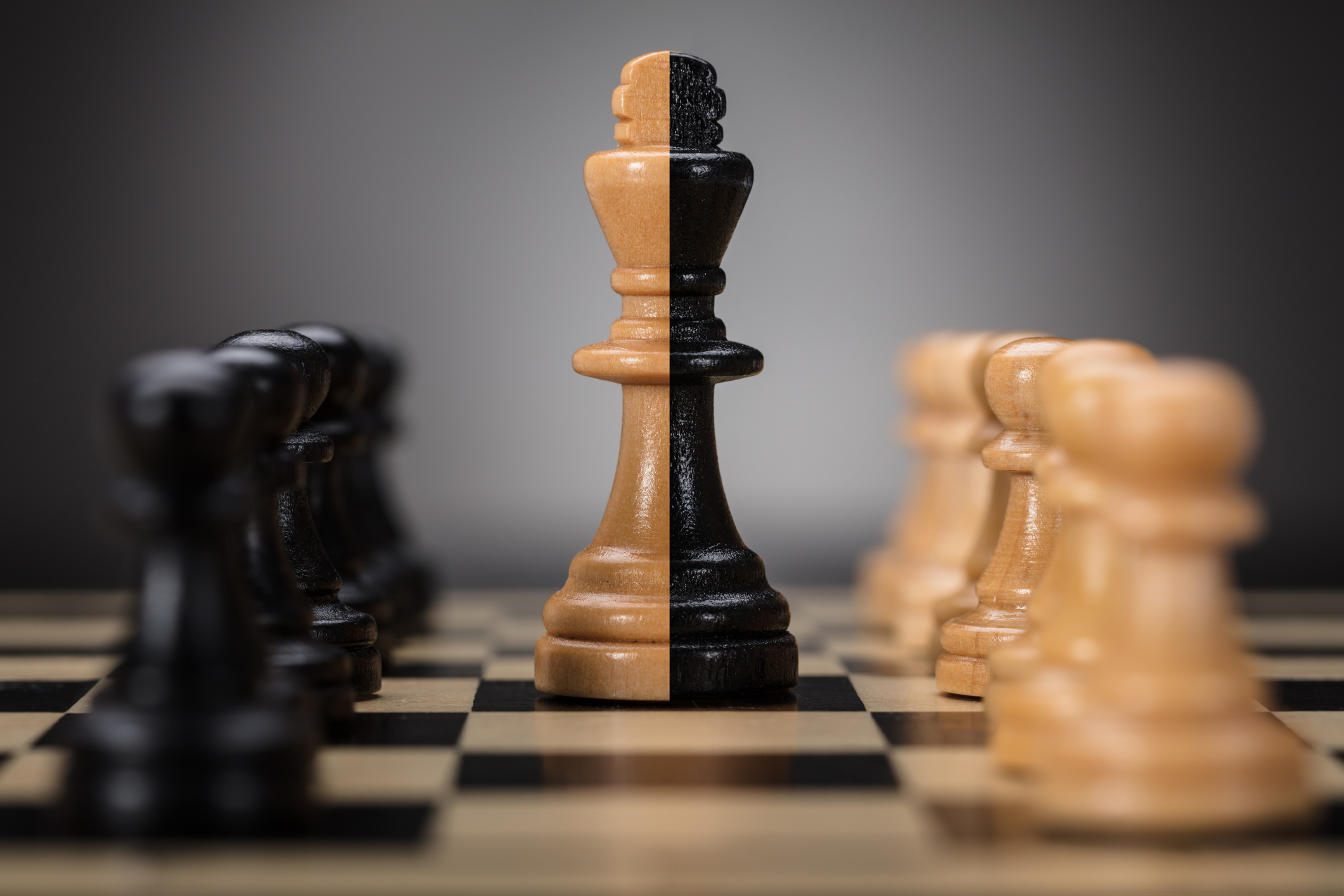 Pawn chess pieces surrounding a king chess piece made of two colors.
