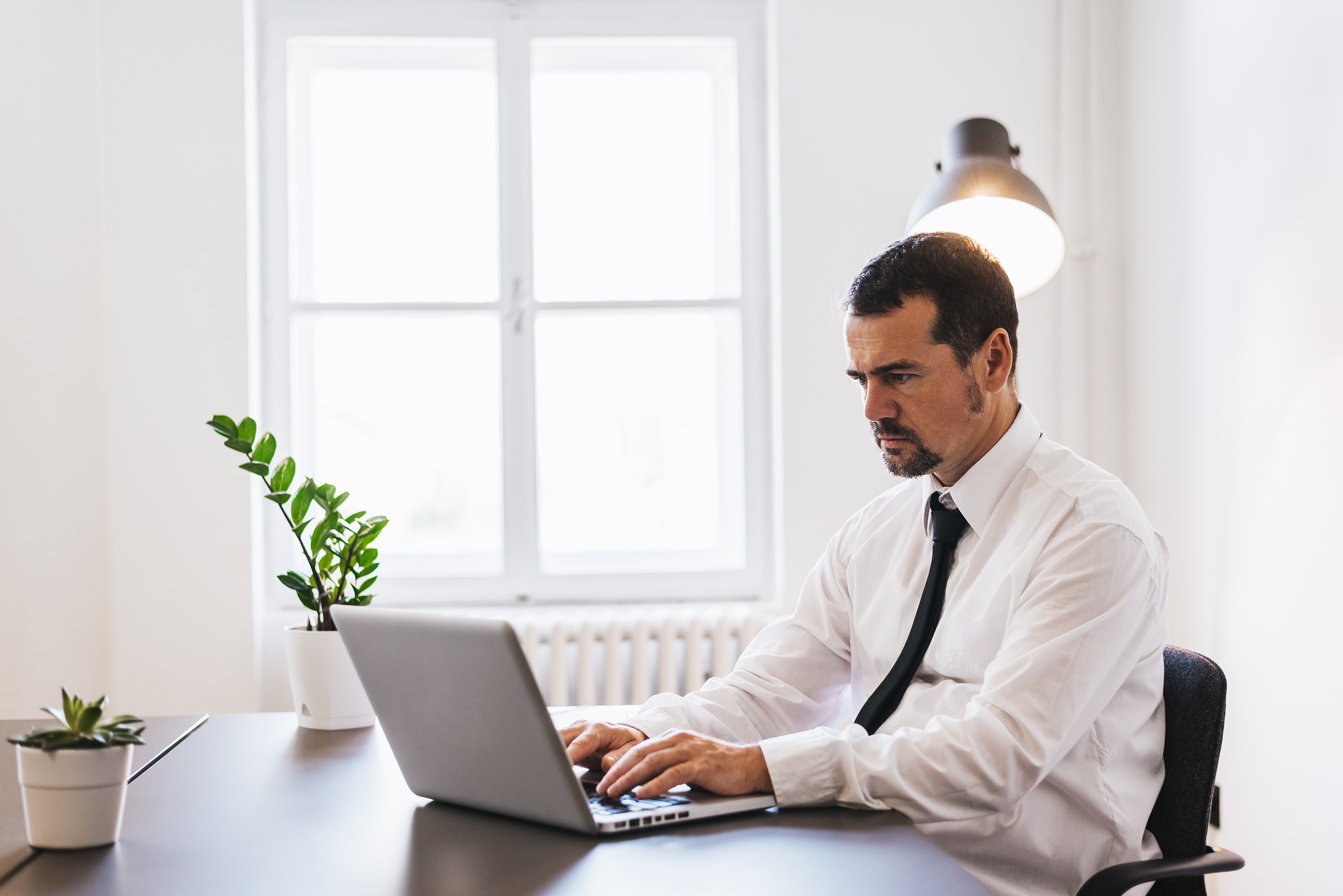Professionally dressed man at laptop with serious expression