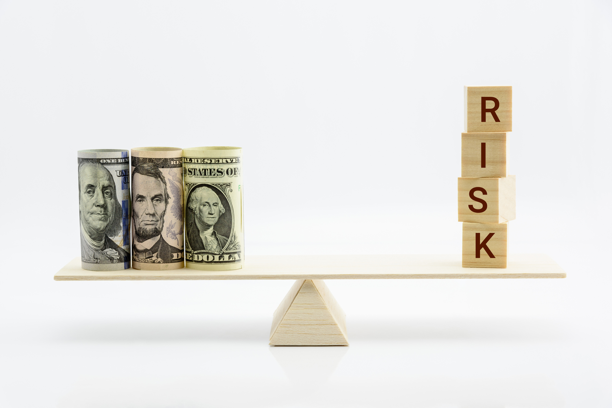 A scale with rolled-up cash on one side and blocks spelling out risk on the other.