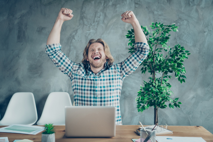 A man cheering after viewing his laptop.