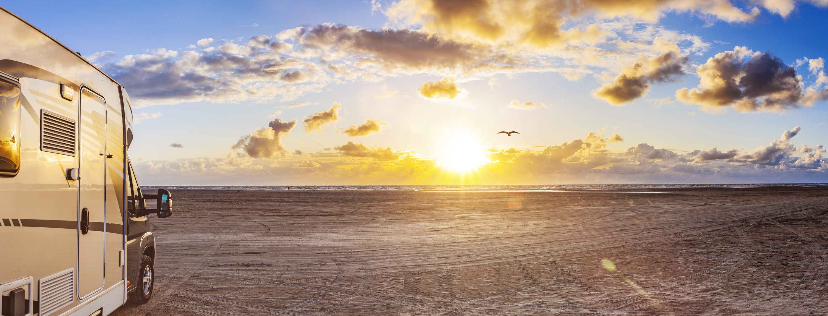 A recreational vehicle is parked on a beach at sunset.