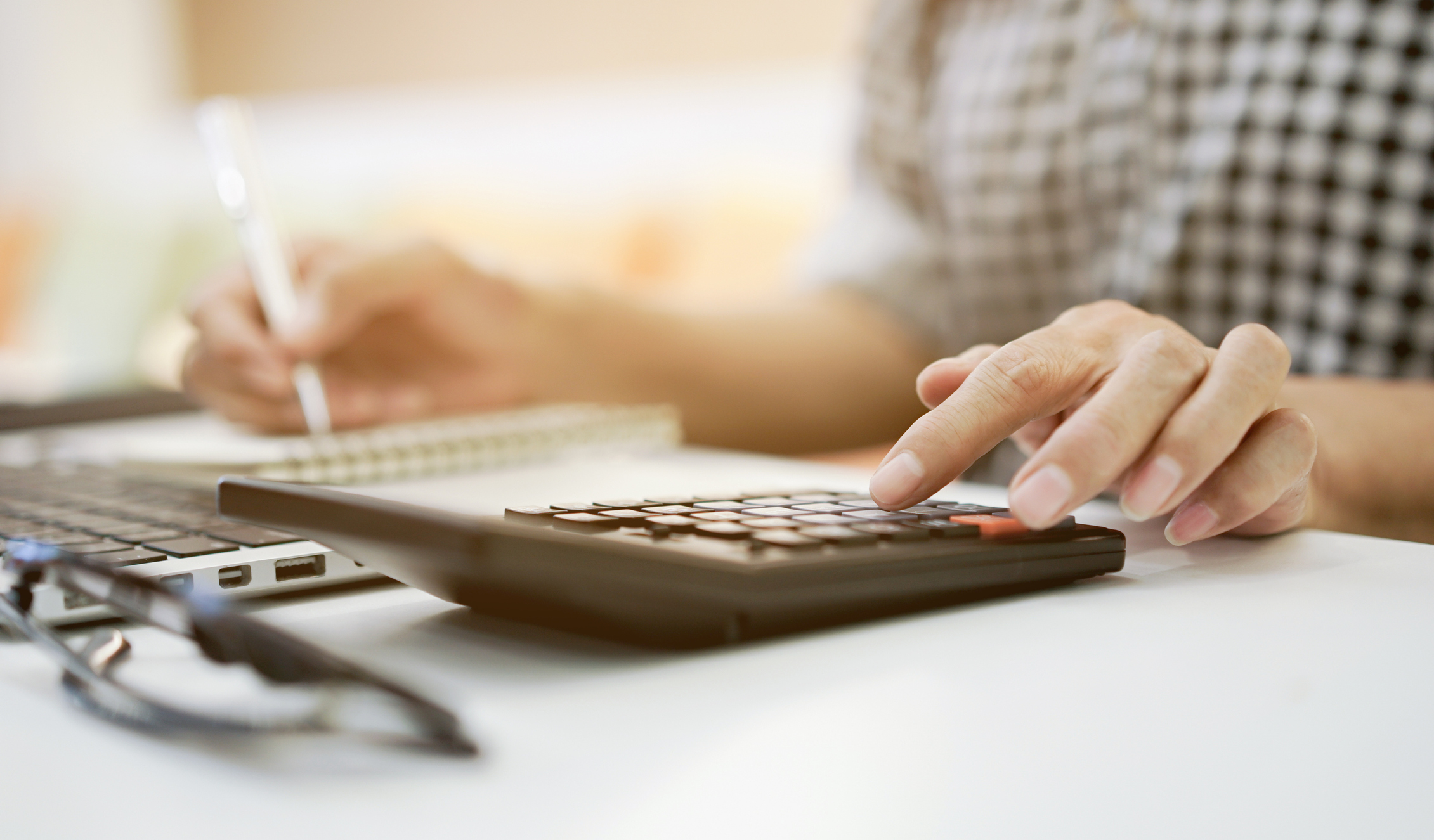 A person sitting at a desk holds a pen in one hand and uses a calculator with the other.