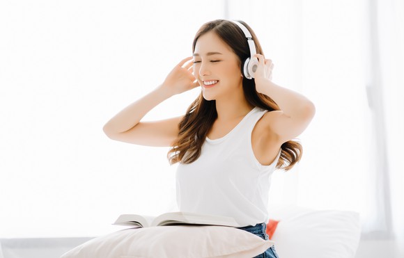 A smiling young woman listens to music through headphones.