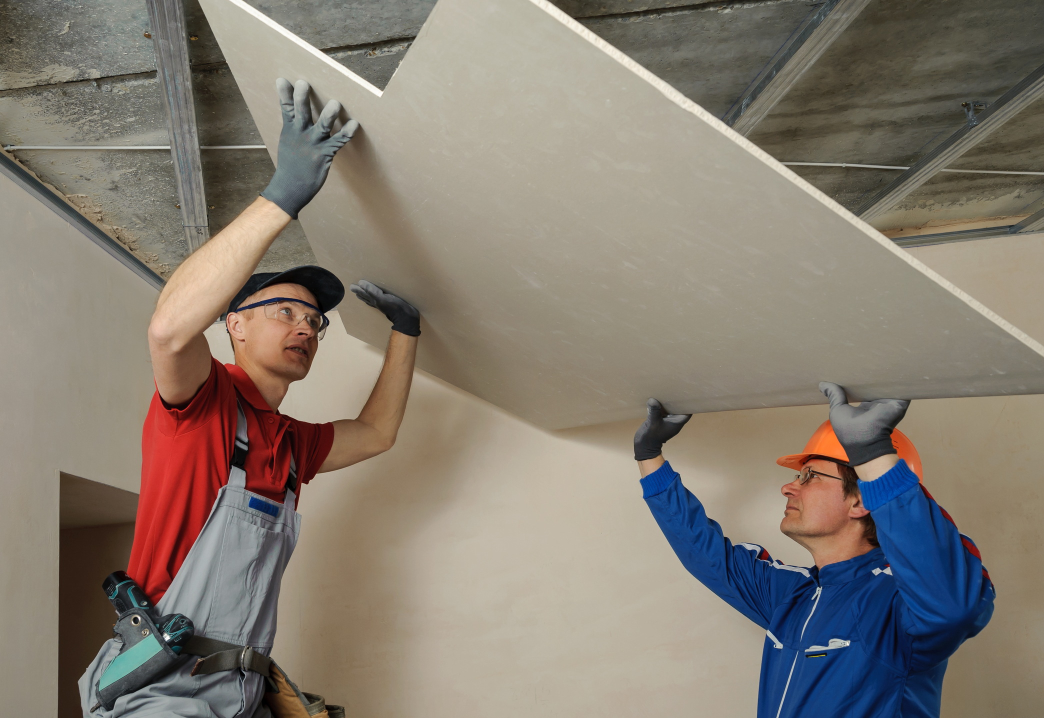 Two contractors installing drywall on the ceiling.