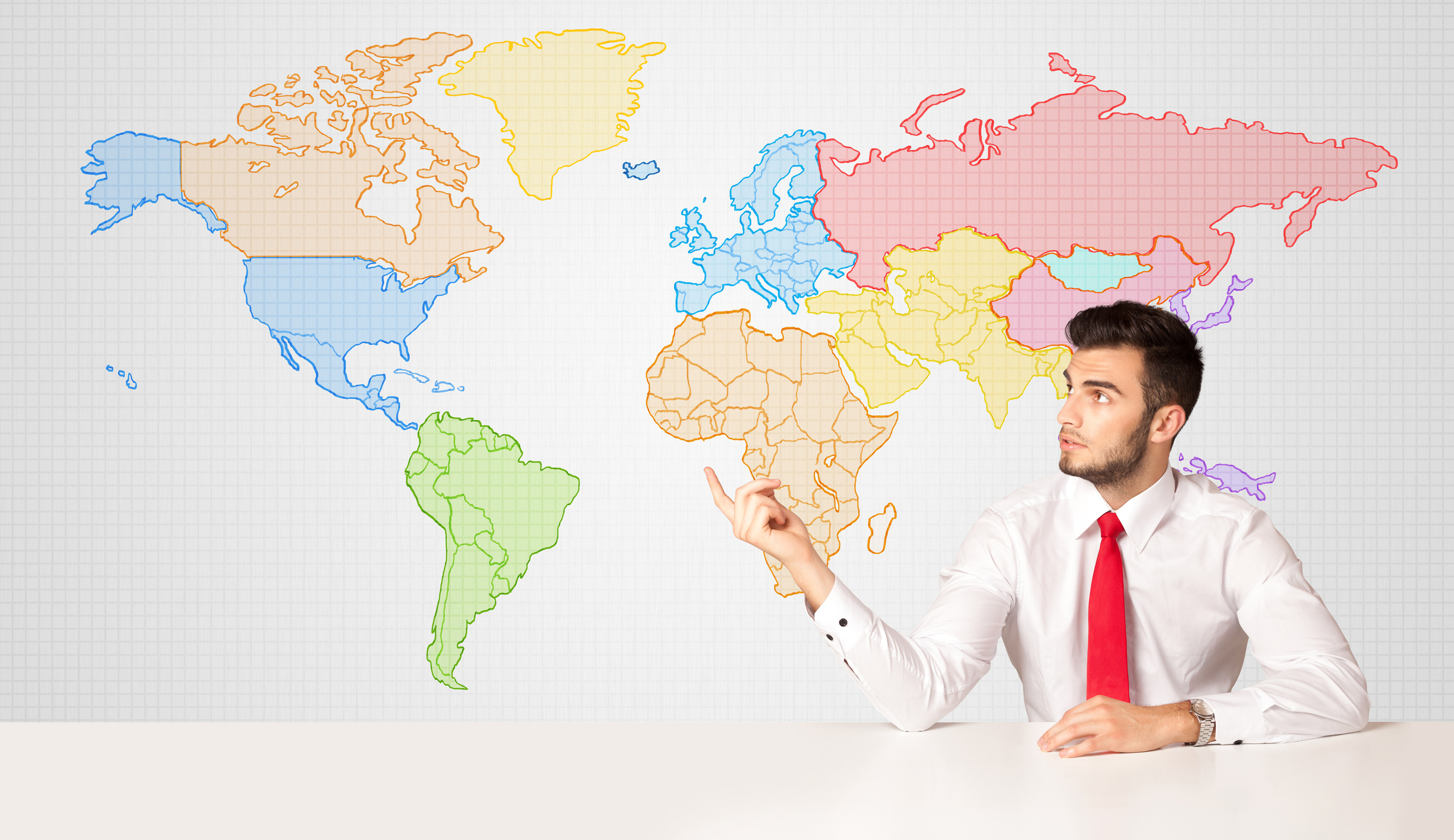 Man in white shirt and red tie sits in front of a large world map.