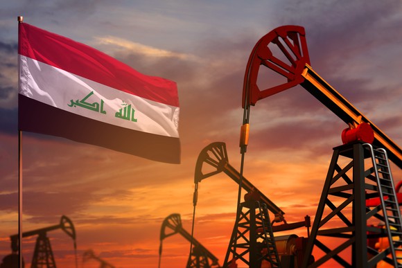 Oil pumps and an Iraqi flag with the sun setting in the background.