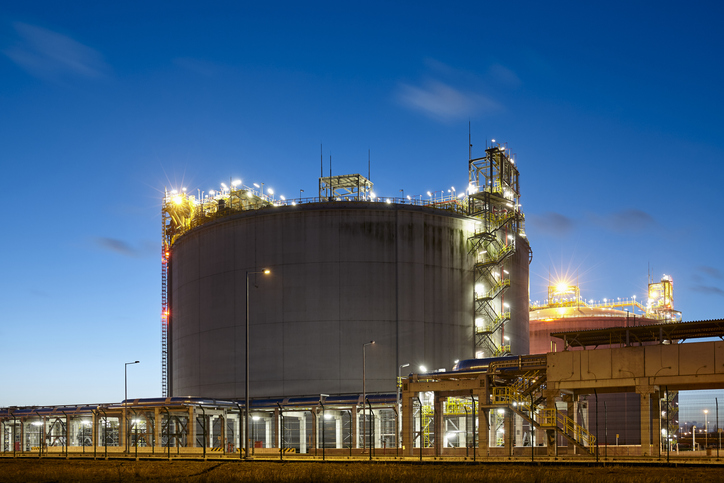 A natural gas storage tank surrounded by lights at dusk