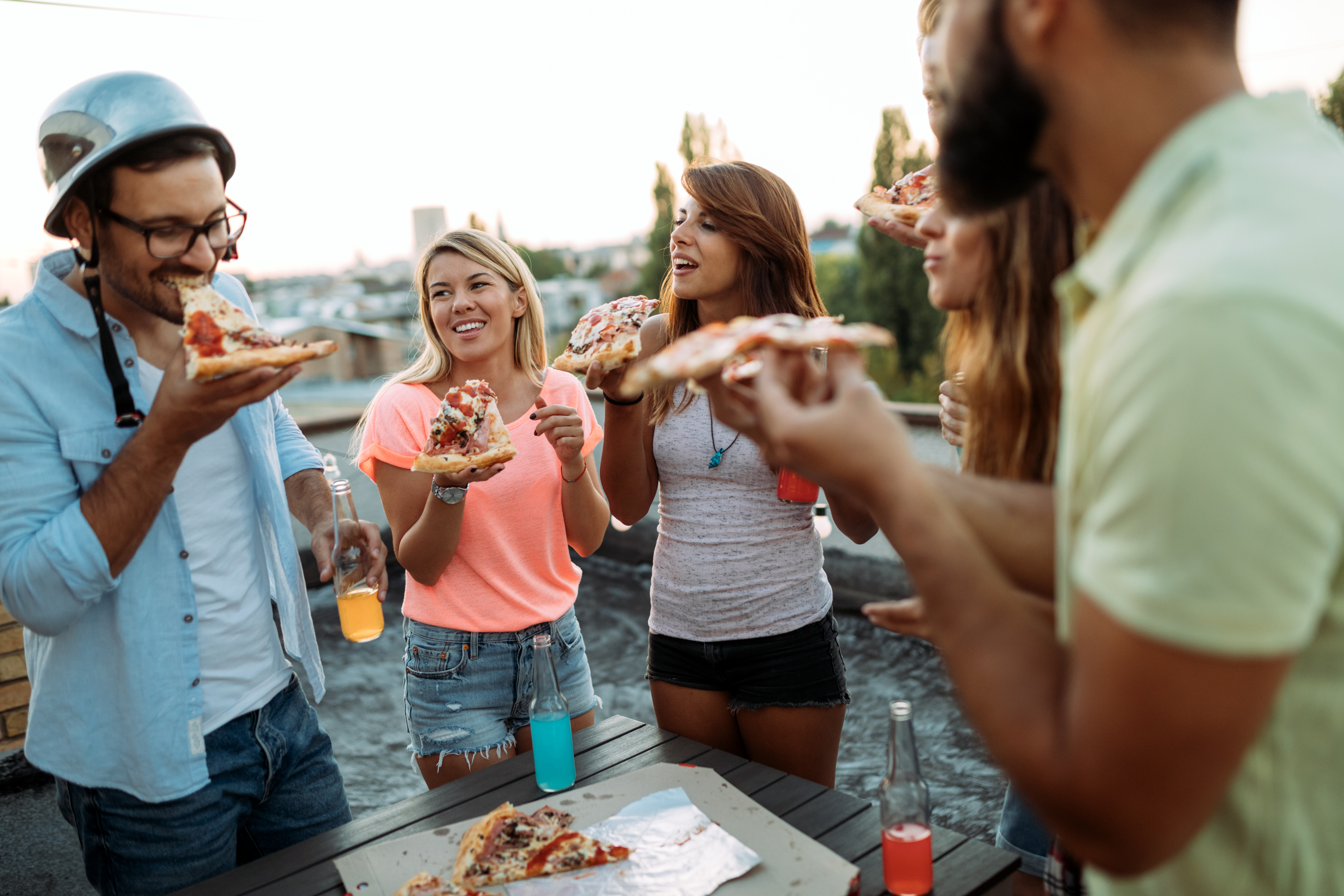Friends enjoy pizza on a rooftop patio.