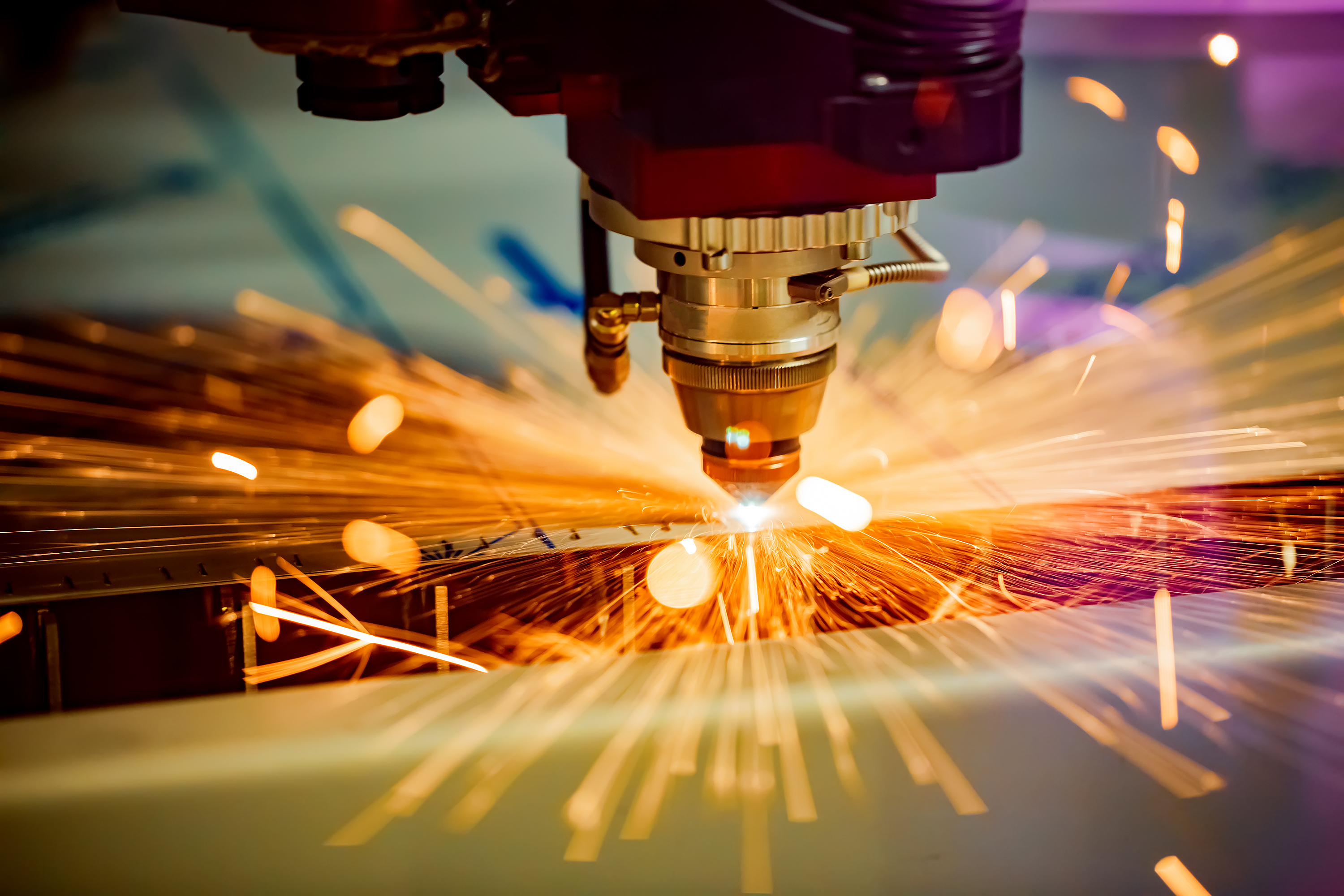 A laser cuts a piece of metal, sending sparks flying.