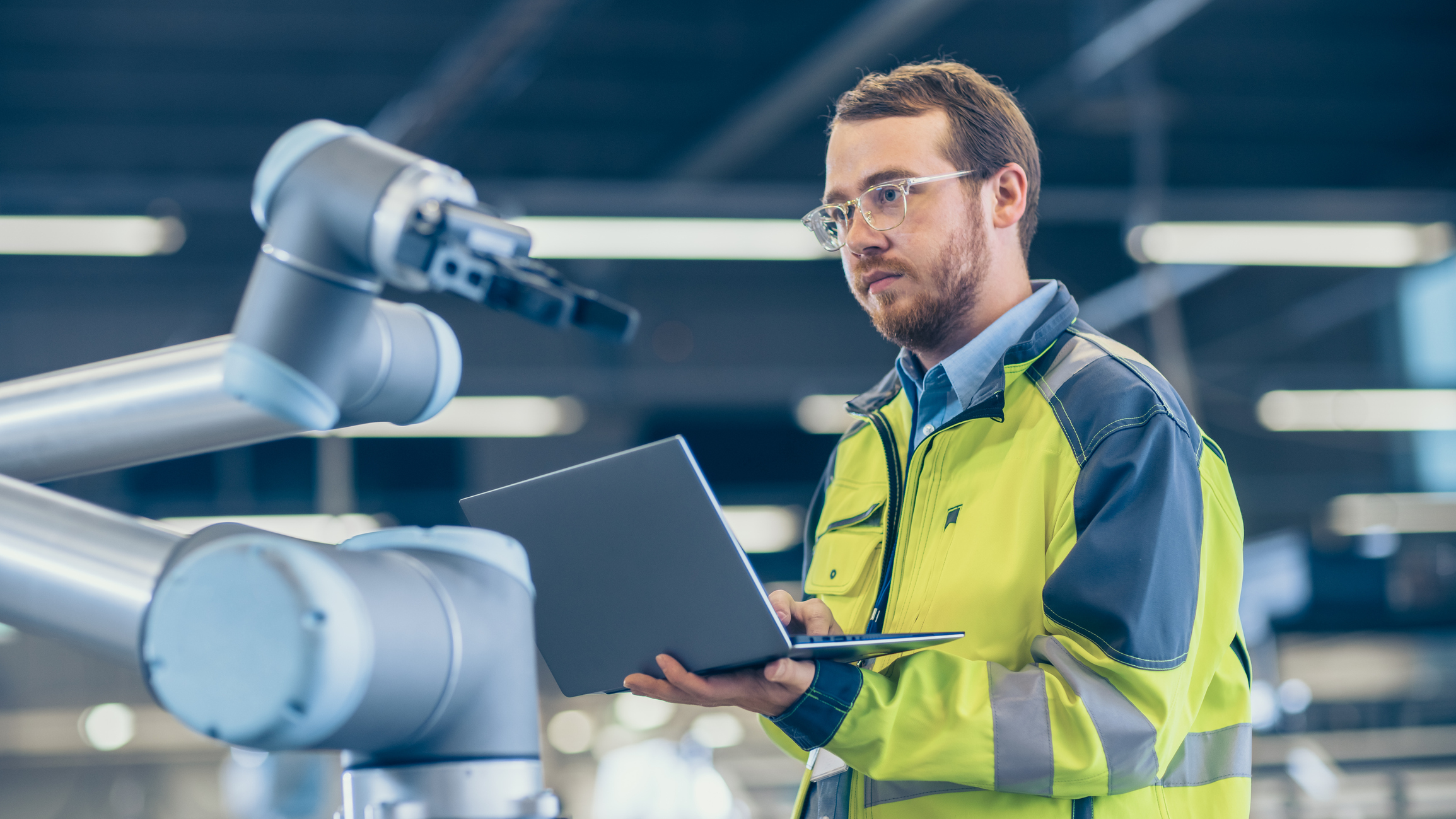 Photograph of man using a laptop to program a mechanical robotic arm