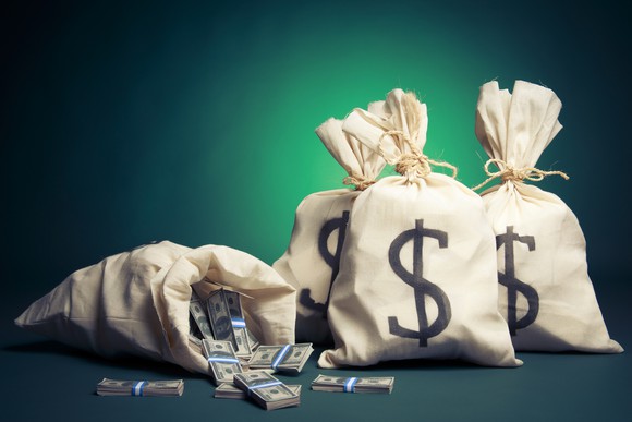 Four bags of money, with dollar signs on them, are shown -- one has tipped over, with cash falling out. 