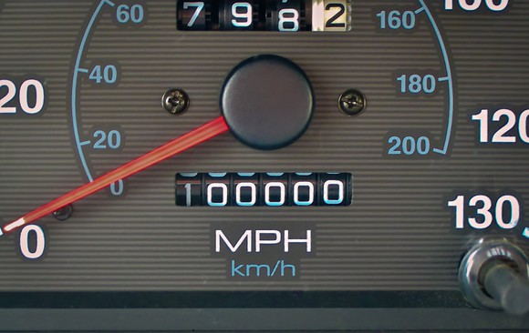 We see a close-up of a car's odometer, at 100,000 miles, is shown.