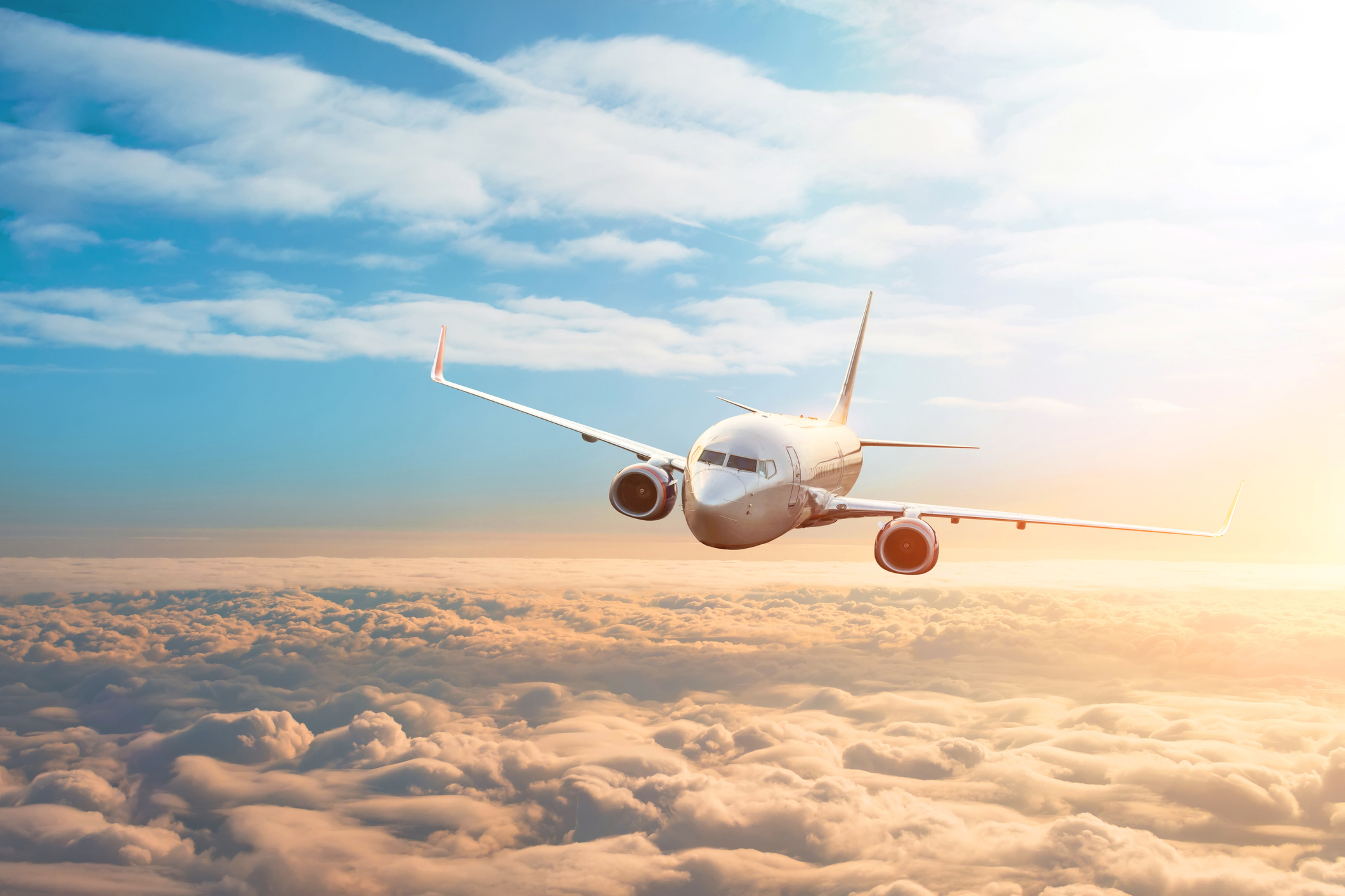A passenger plane flies over a sunset sky.