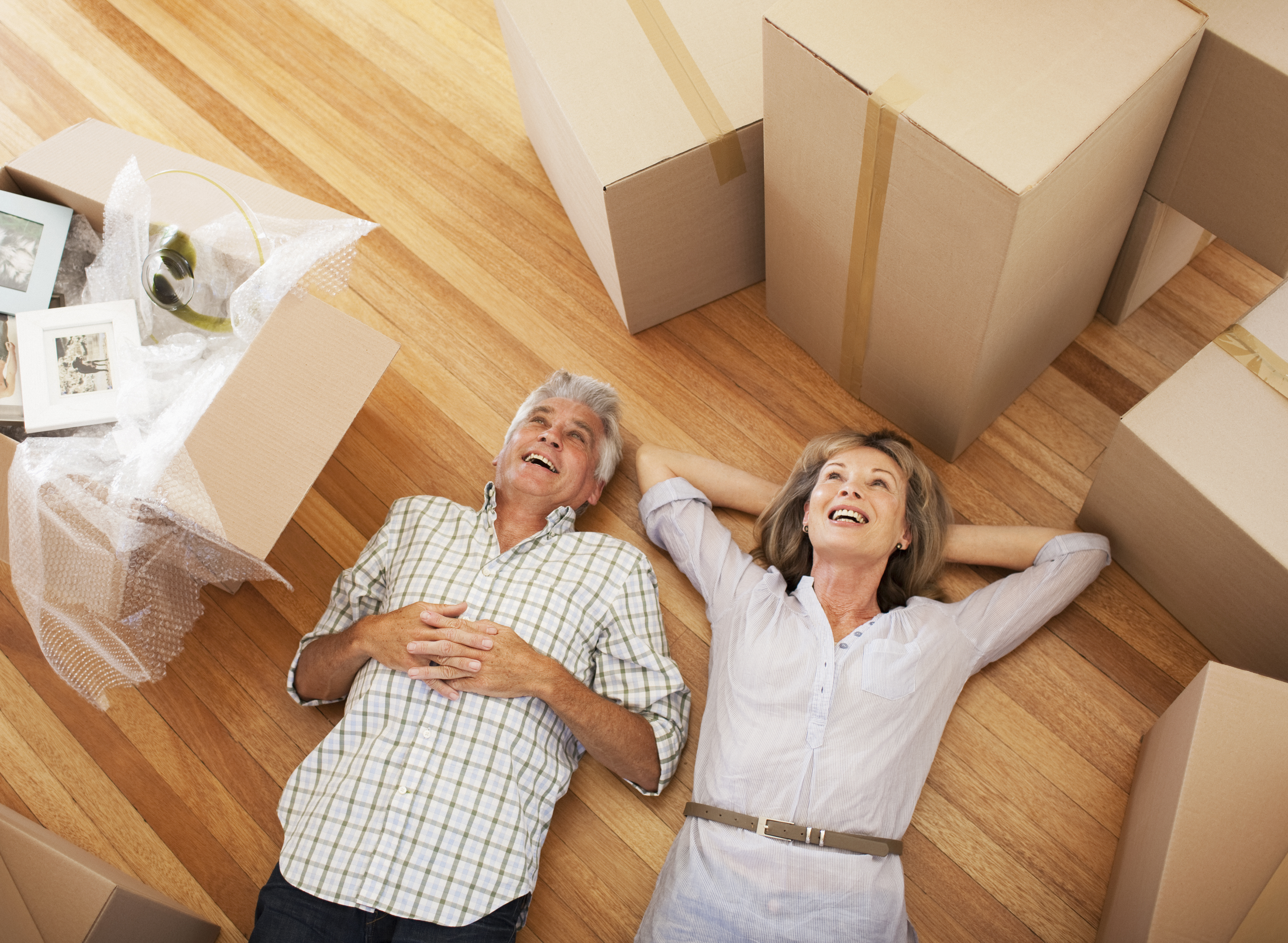 Older couple laying on floor in the middle of moving boxes.