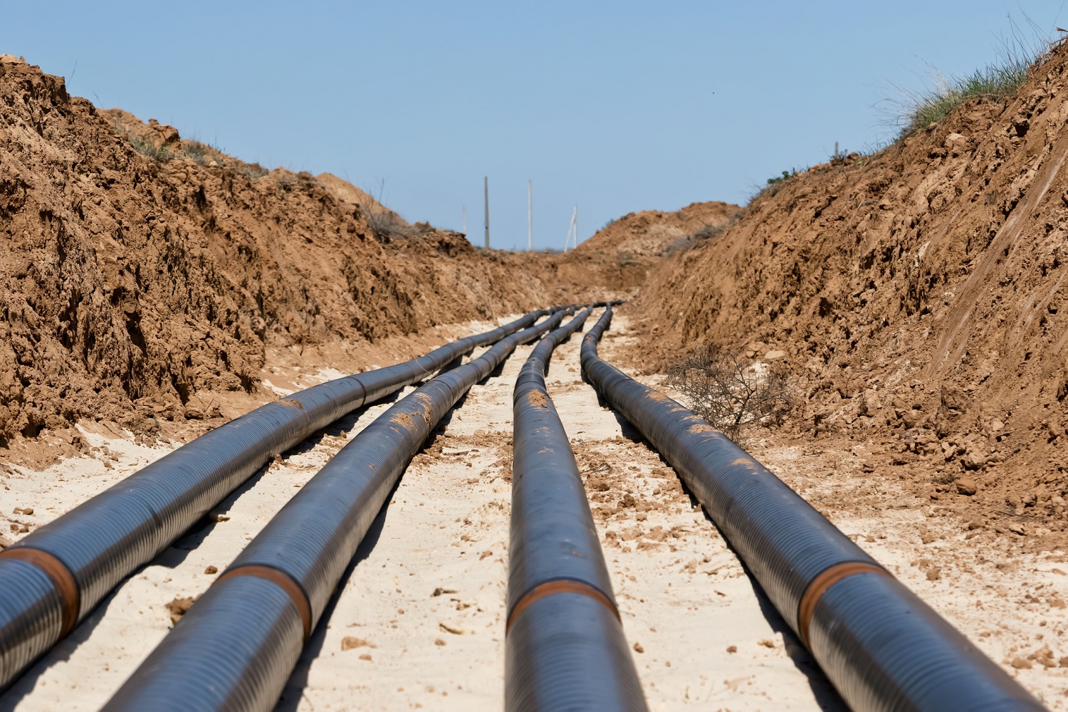 Four pipelines running through a dirt trench.