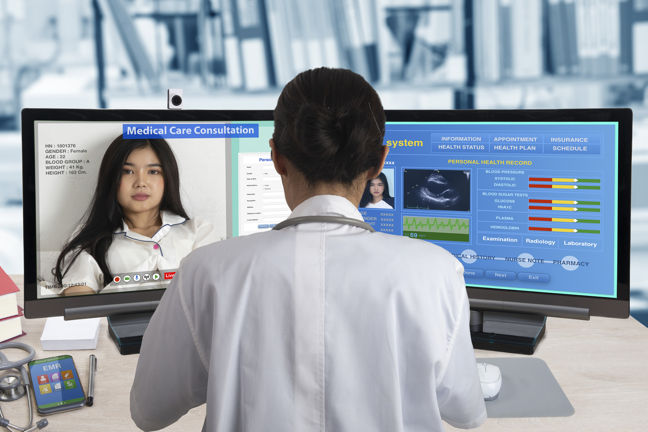 A doctor sitting in front of two computer monitors while chatting remotely with a patient.