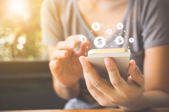 Woman using a smartphone with dollar signs appearing above the phone.