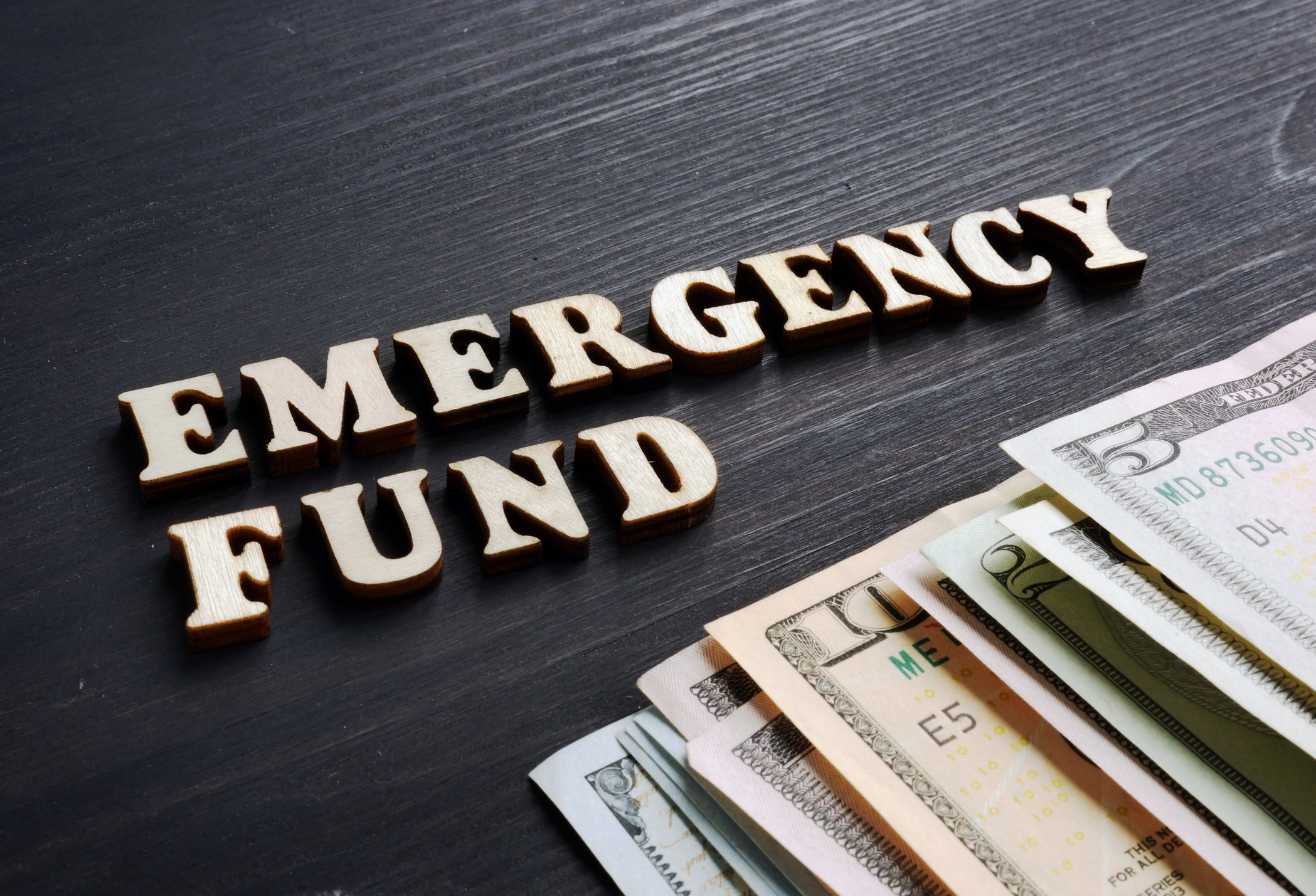 The words 'emergency fund' on a table next to various denominations of bills.