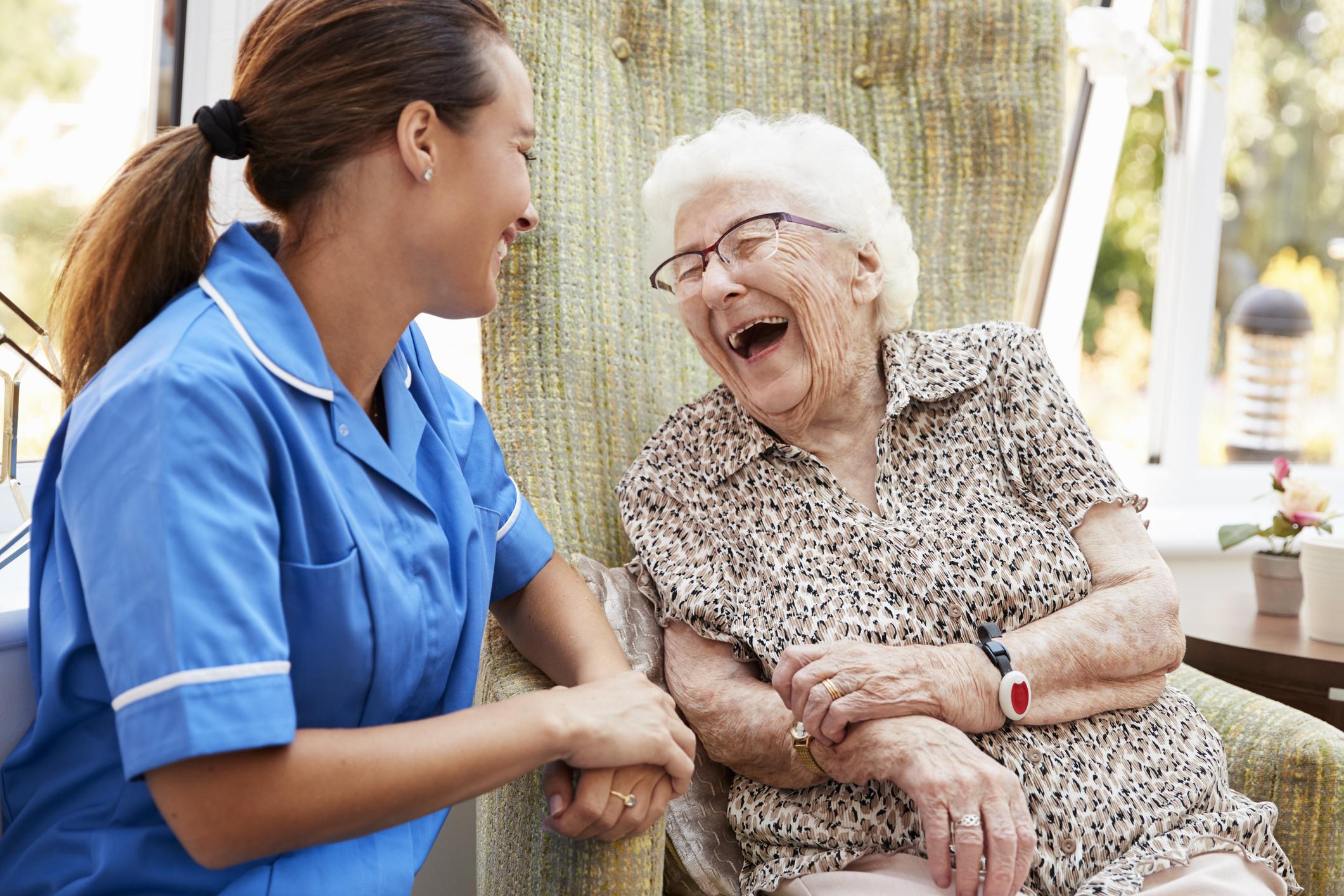 Young woman in scrubs smiling, sitting next to laughing older woman