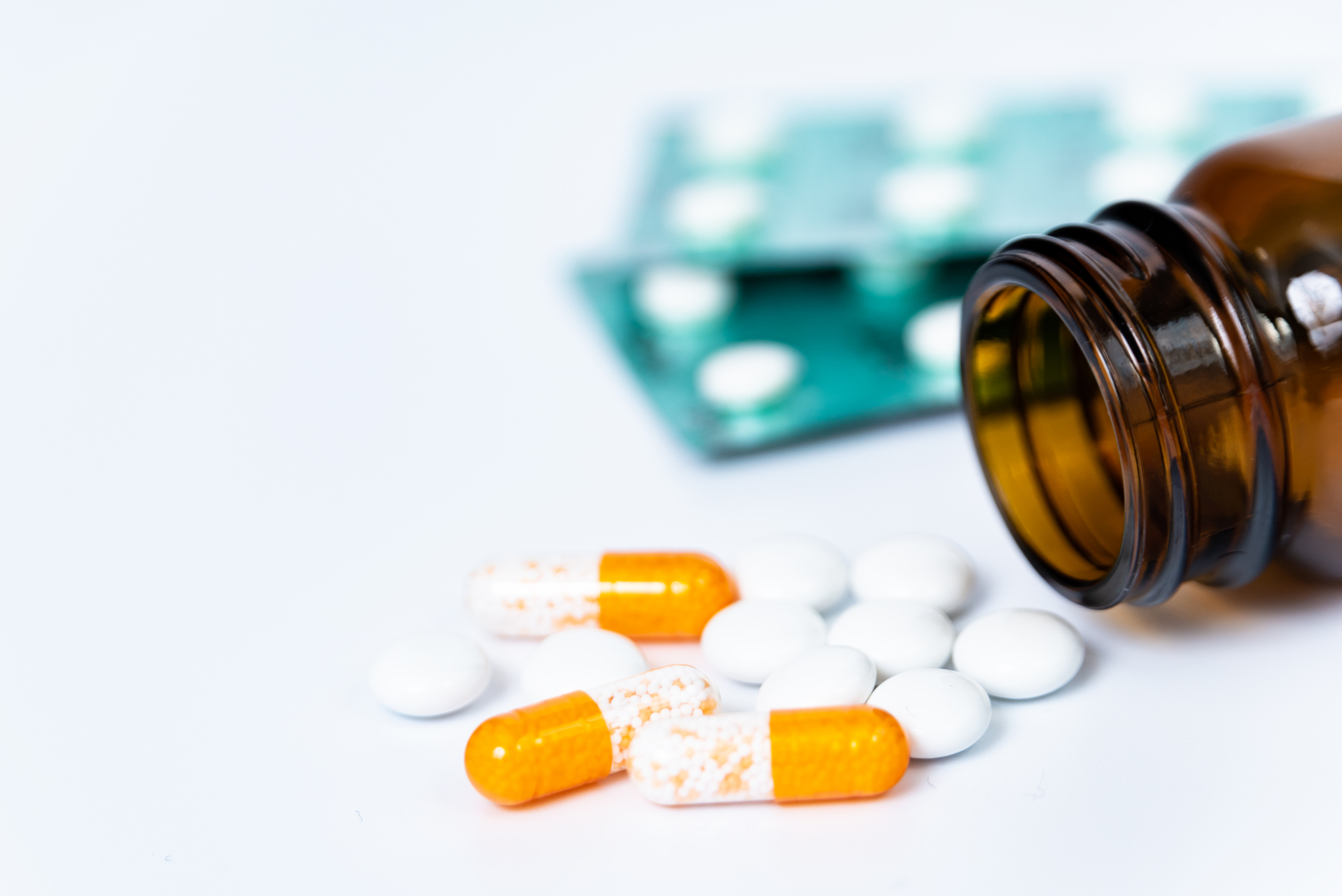 Capsules, pills, a glass medication bottle, and pills in blister packs lying on a surface.