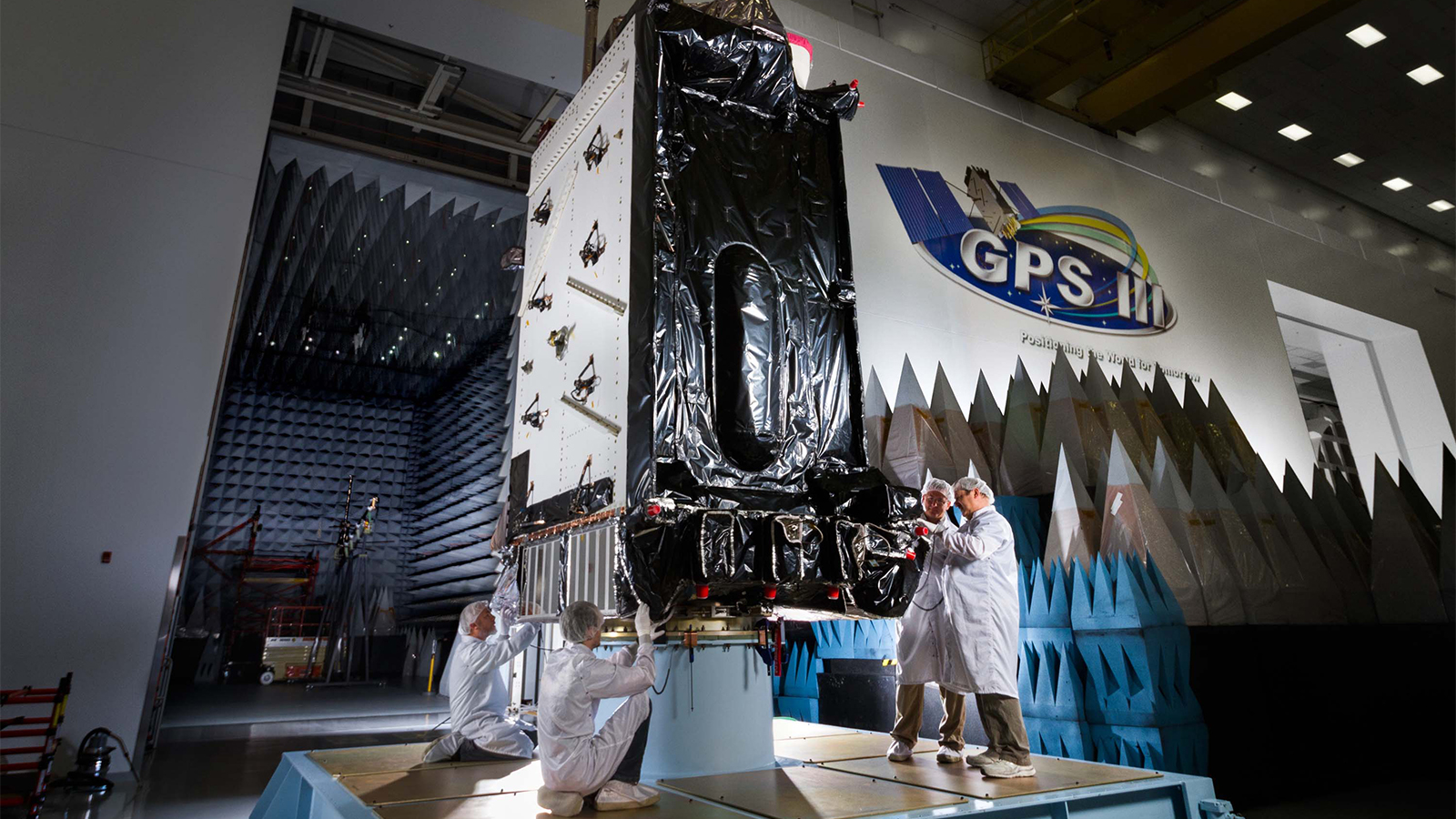 Engineers work on a GPS satellite in a production facility.