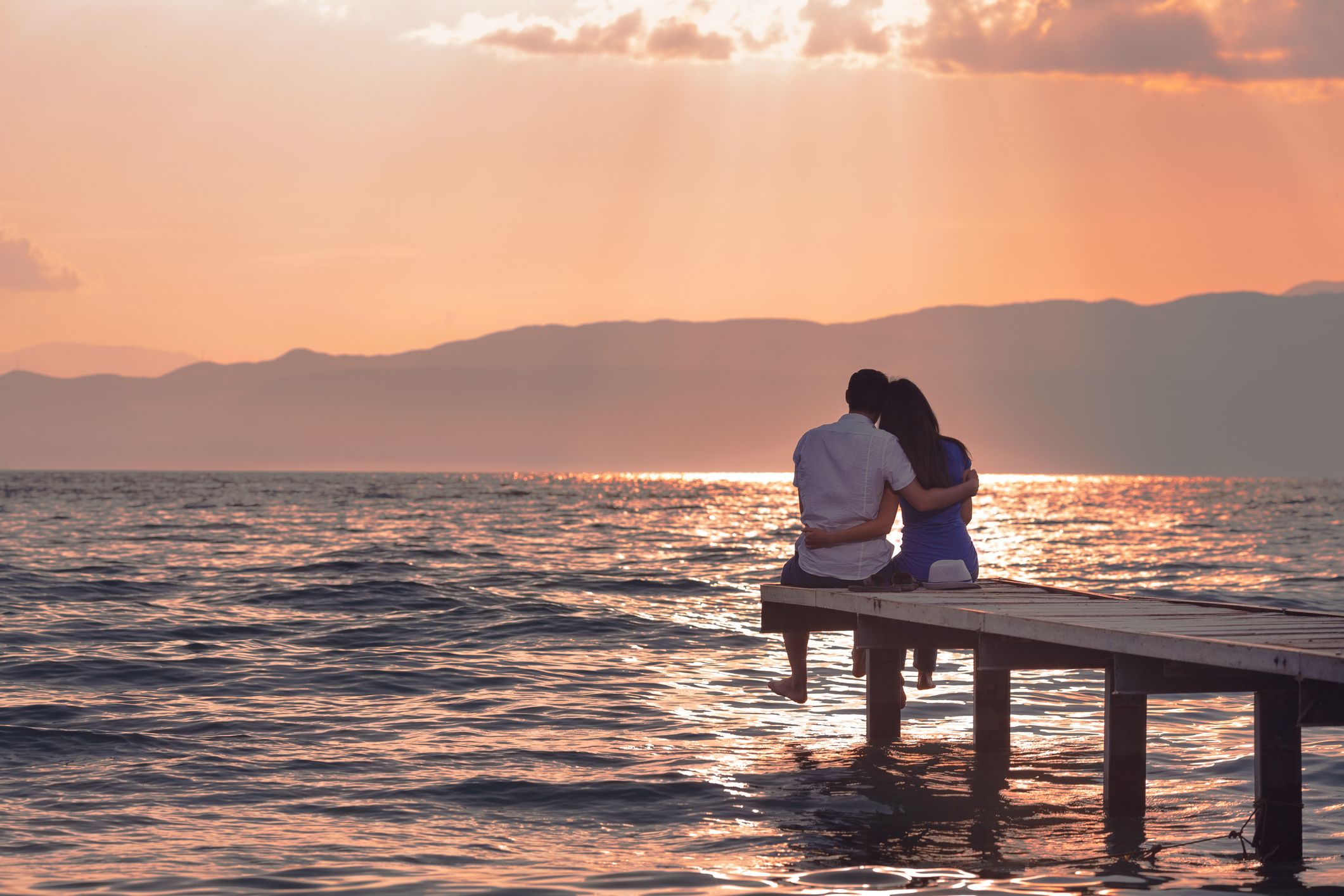 Couple sitting on a dock watching a sunset