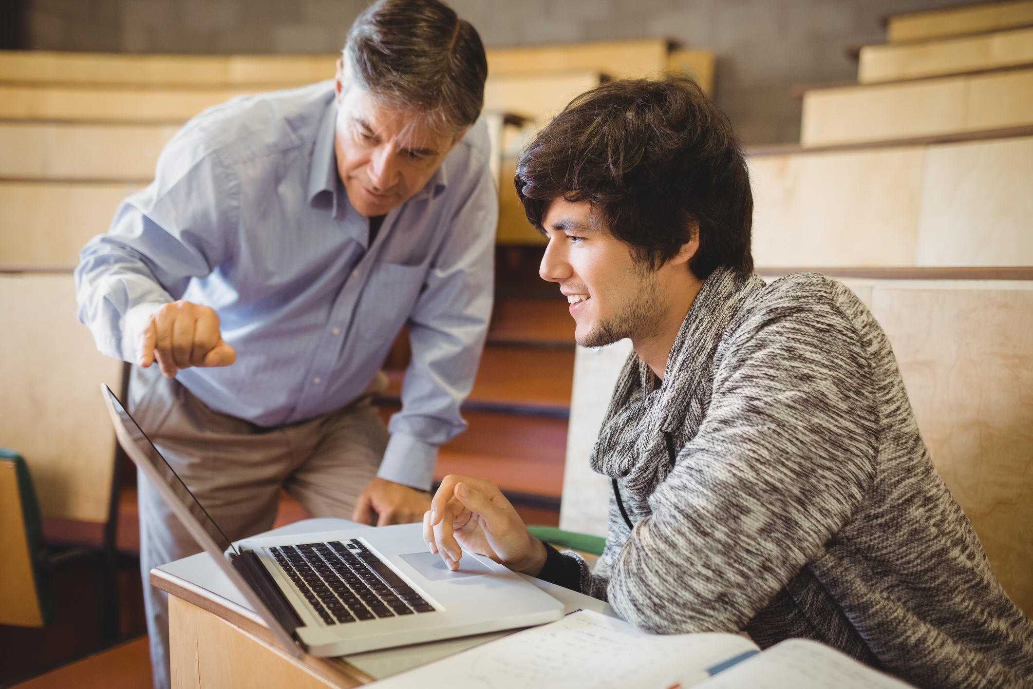 Older man pointing to laptop while younger man sits at it
