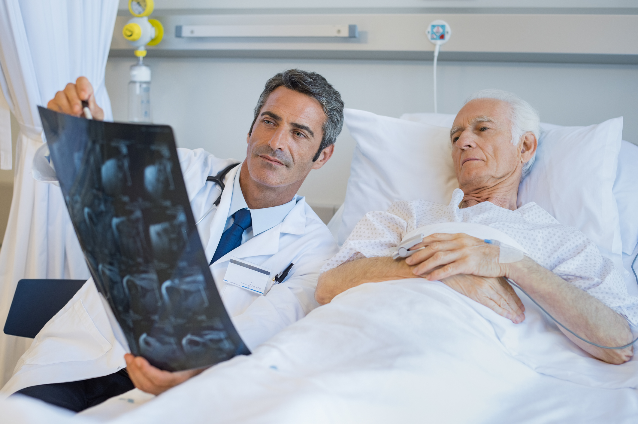 Doctor holding x-ray reading while older man lying in bed looks on