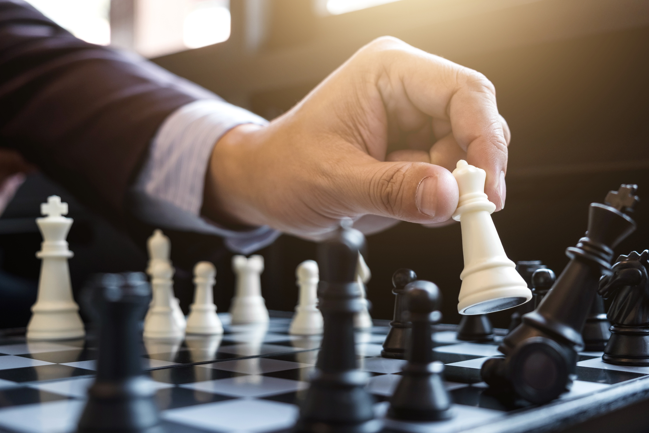 A person moving a white chess piece to knock out a black chess piece.
