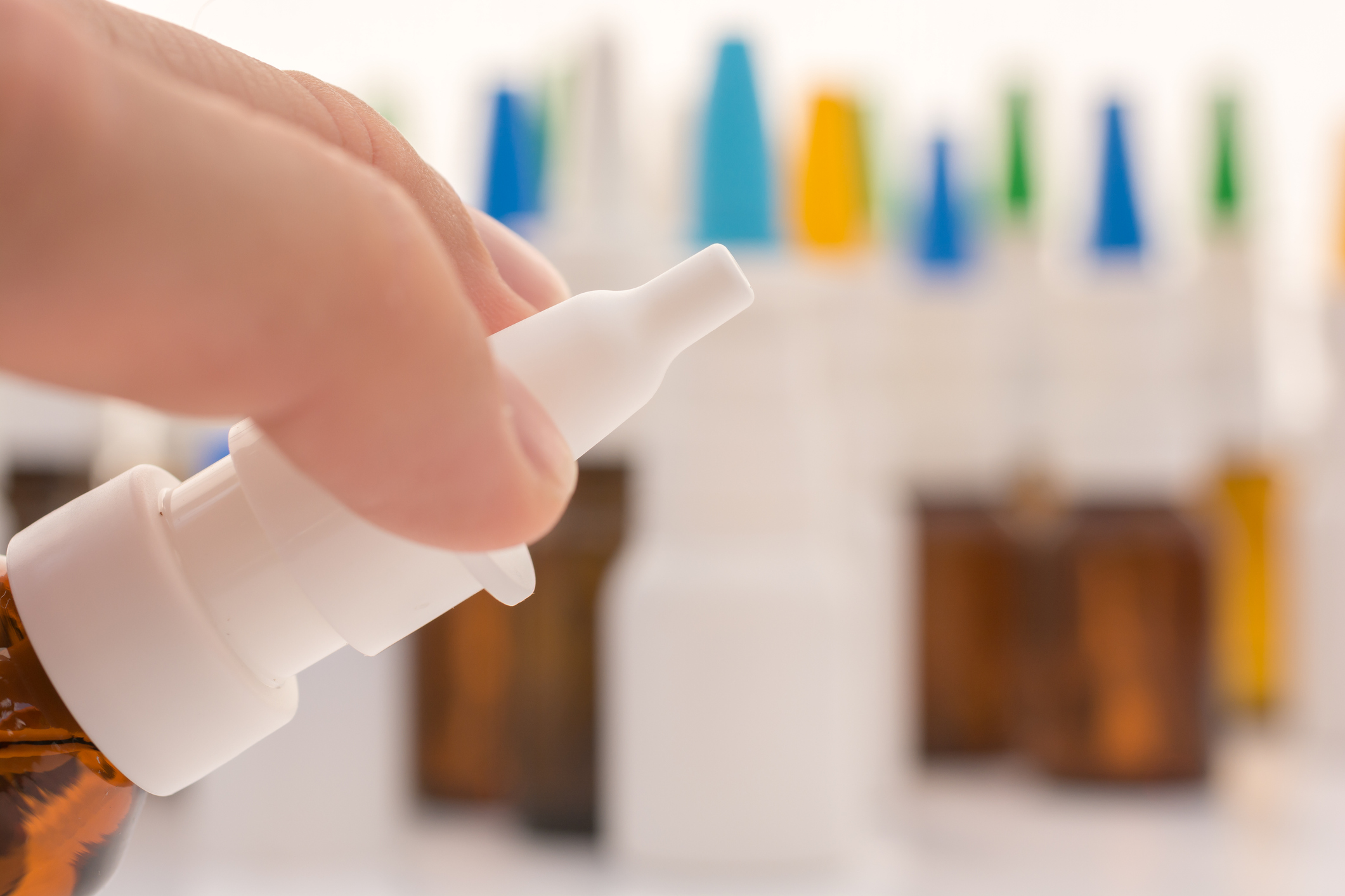A person holding a nasal spray with several other sprays in the background.
