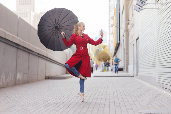 A young woman films herself dancing with an umbrella.