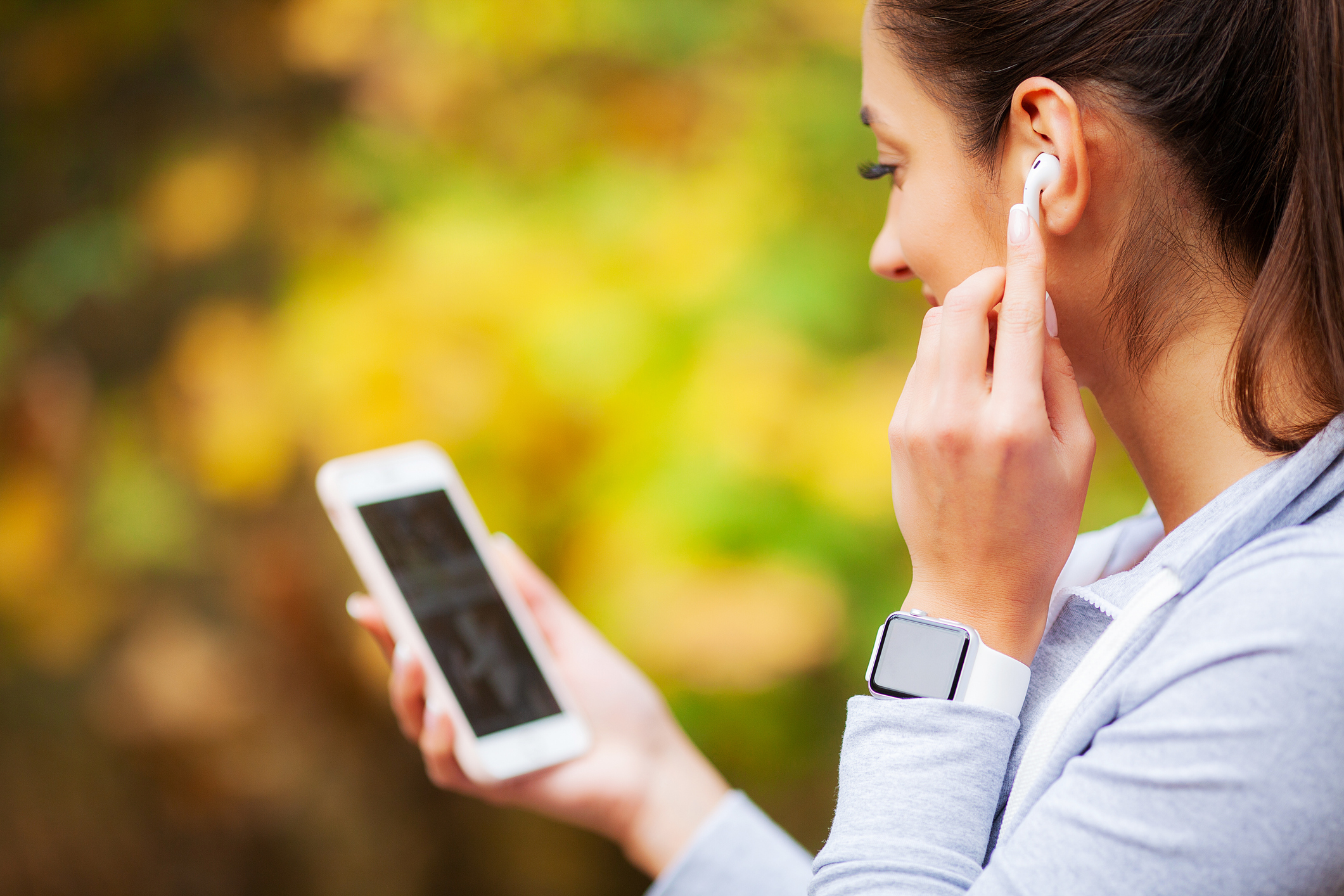 A woman viewing her phone while putting on wireless headphones. 