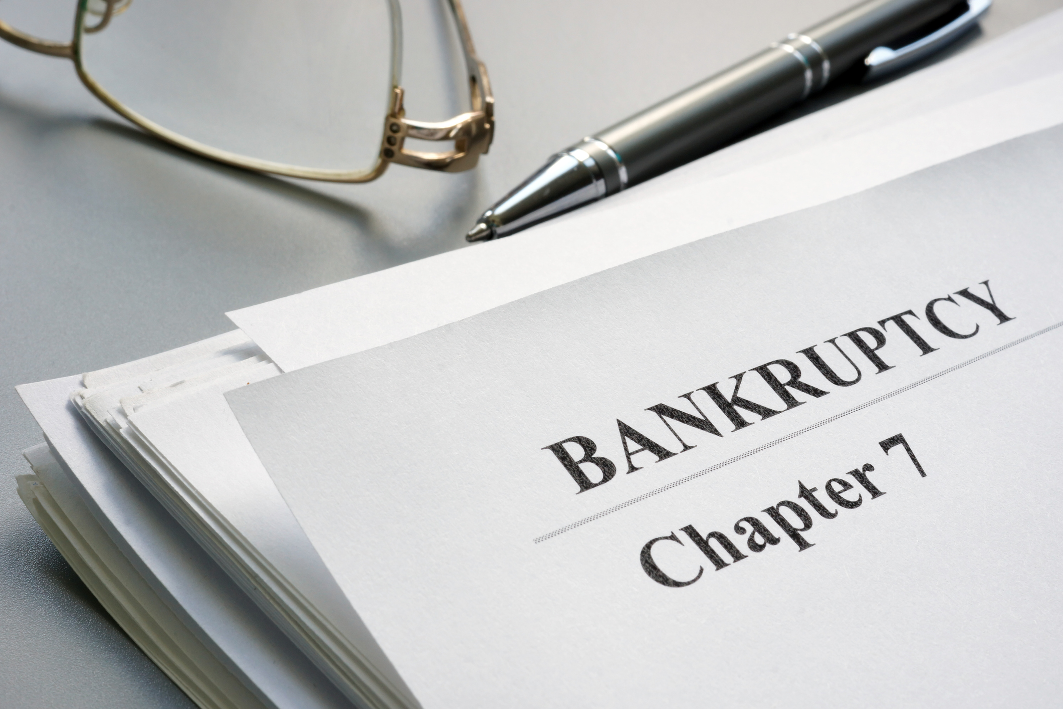 Bankruptcy documents with a pen and some glasses resting on a table.