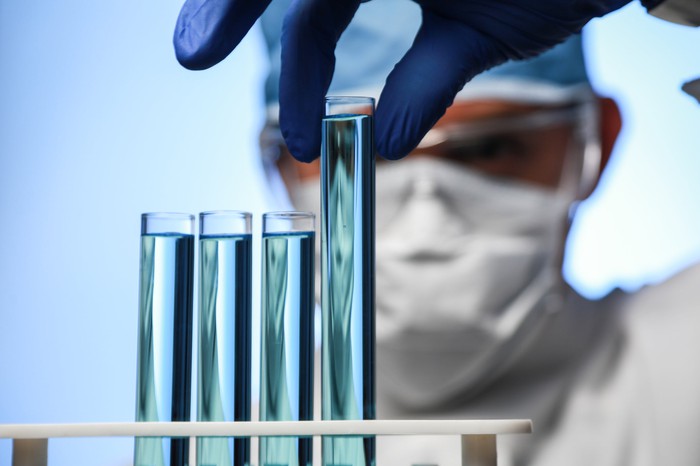 Scientist with mask on holding up a test tube