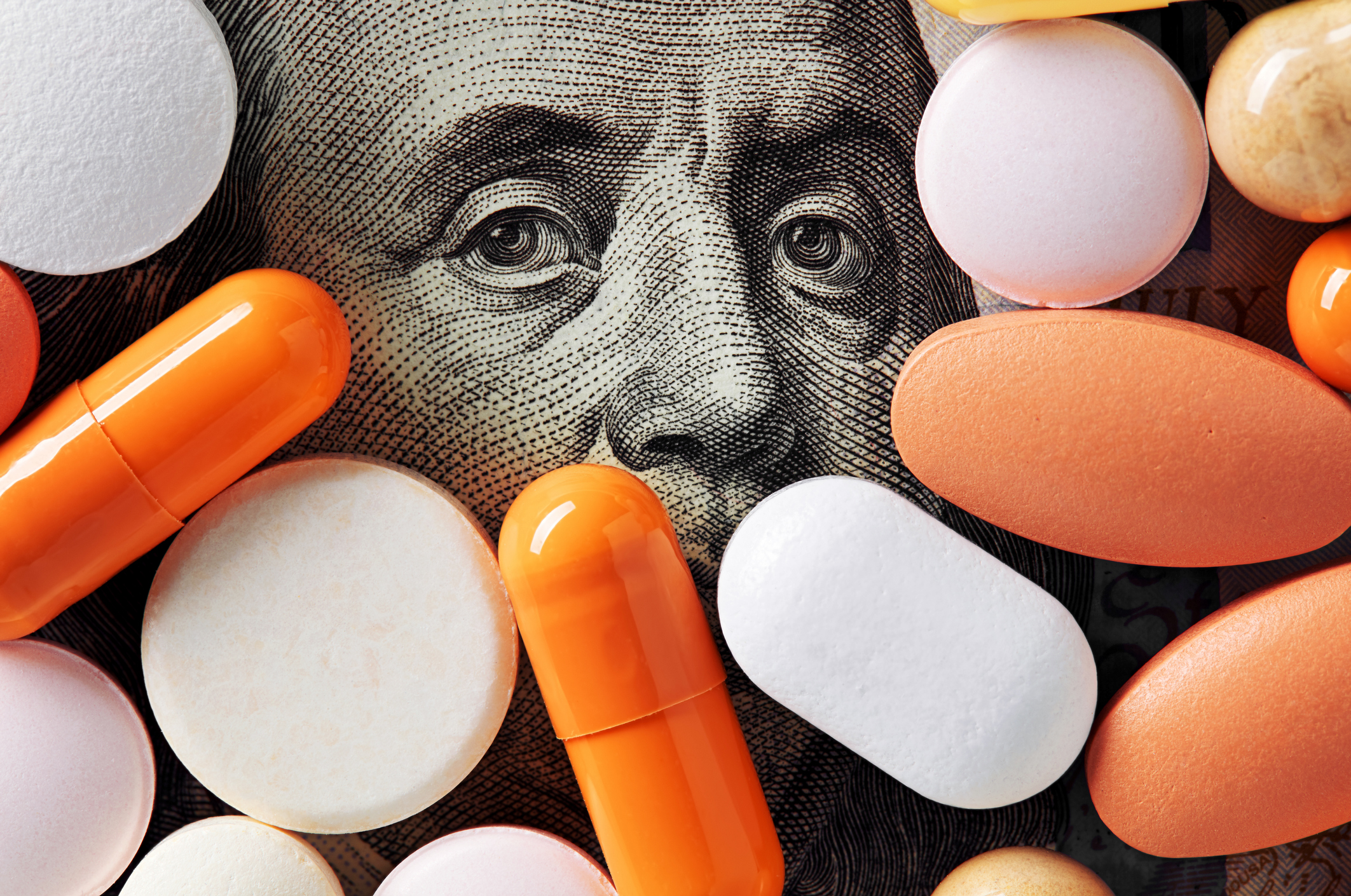 Pills on top of $100 bill with only upper part of Ben Franklin's face showing