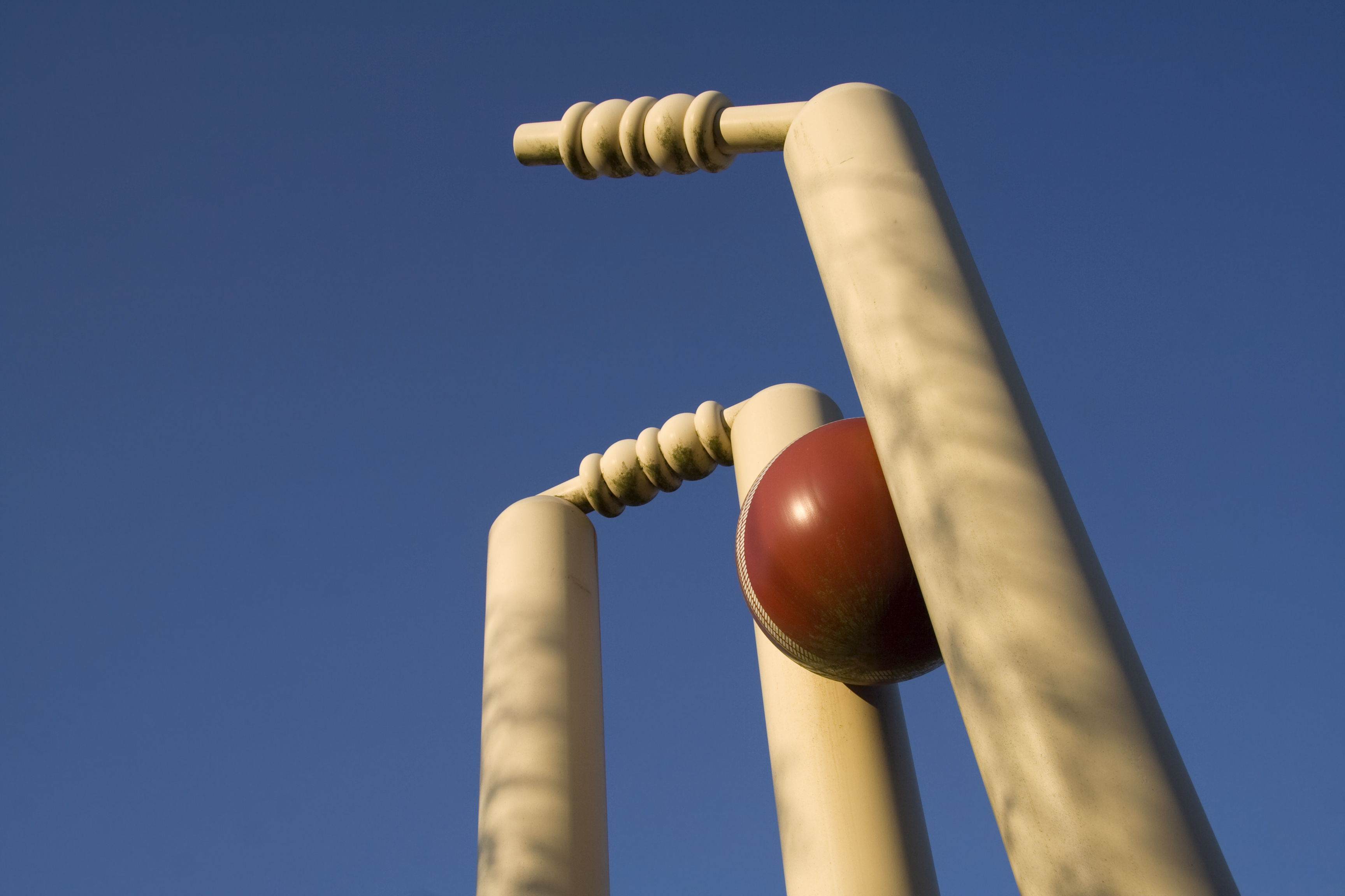 Close-up photo of a cricket ball hitting the wicket.