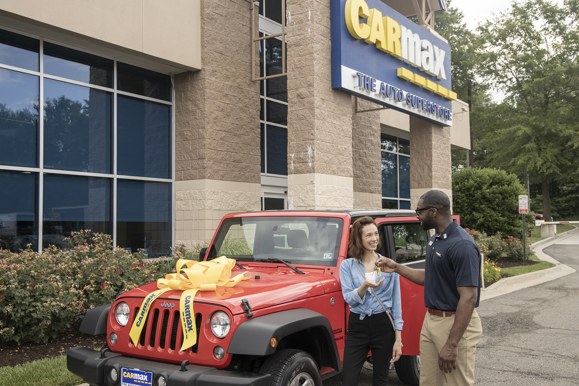 A salesperson handing the keys to a customer's new car in the parking lot of a CarMax store.