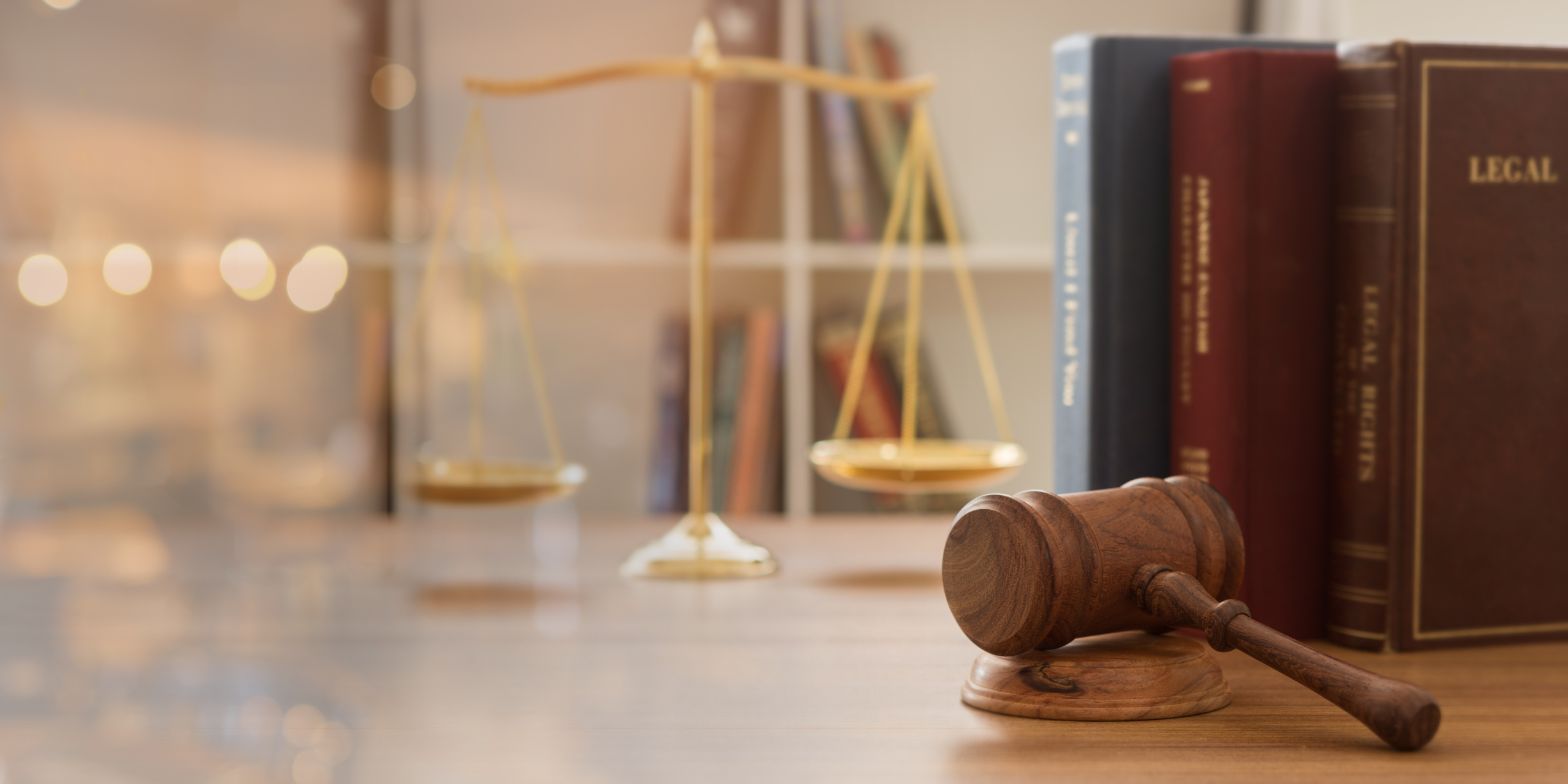 A gavel and hammer, law books, and a scale on a wooden table.