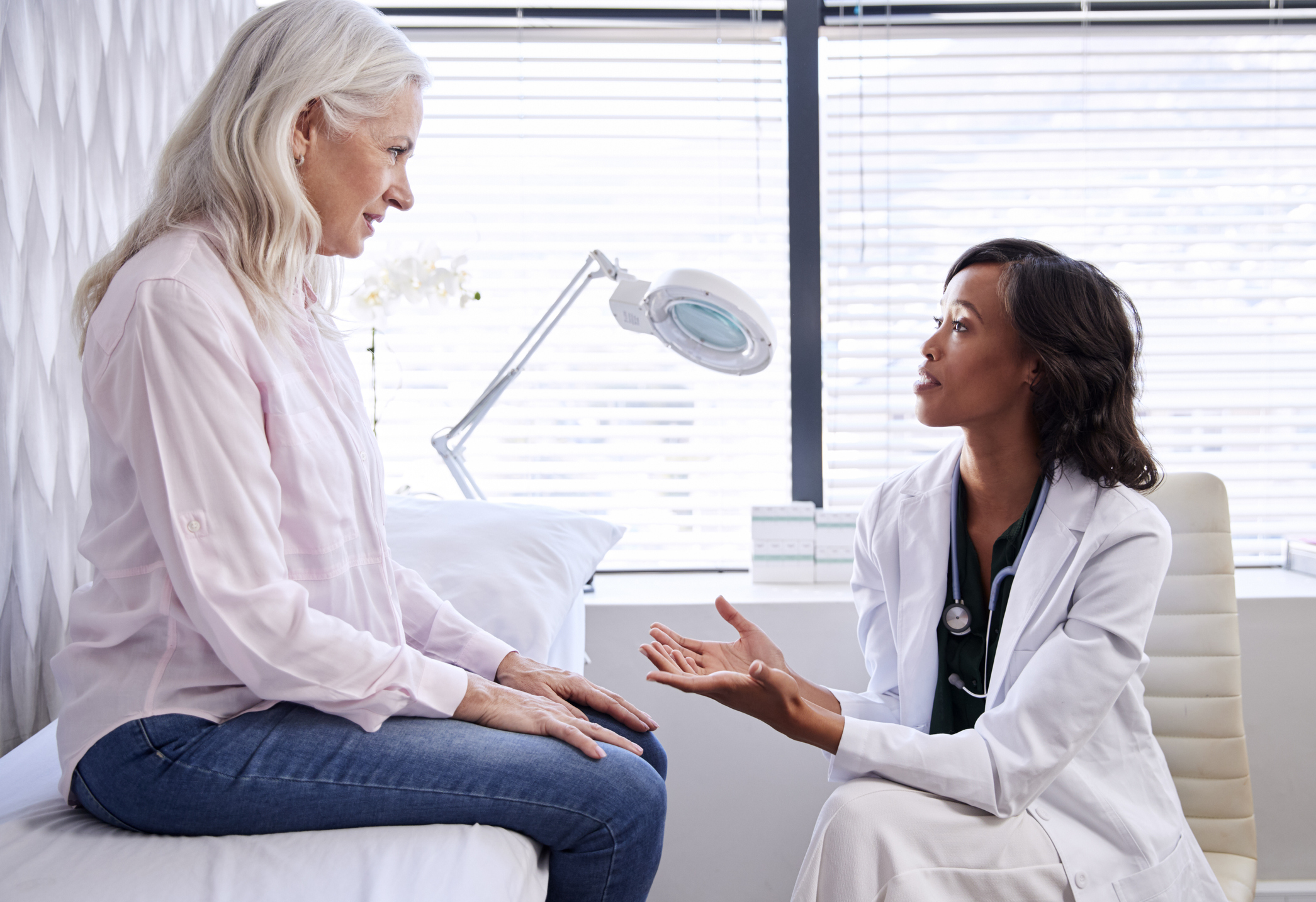 A physician speaks to a woman seated on an exam table.
