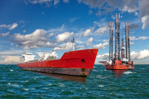 An oil rig and ship pictured next to each other in the middle of the ocean.