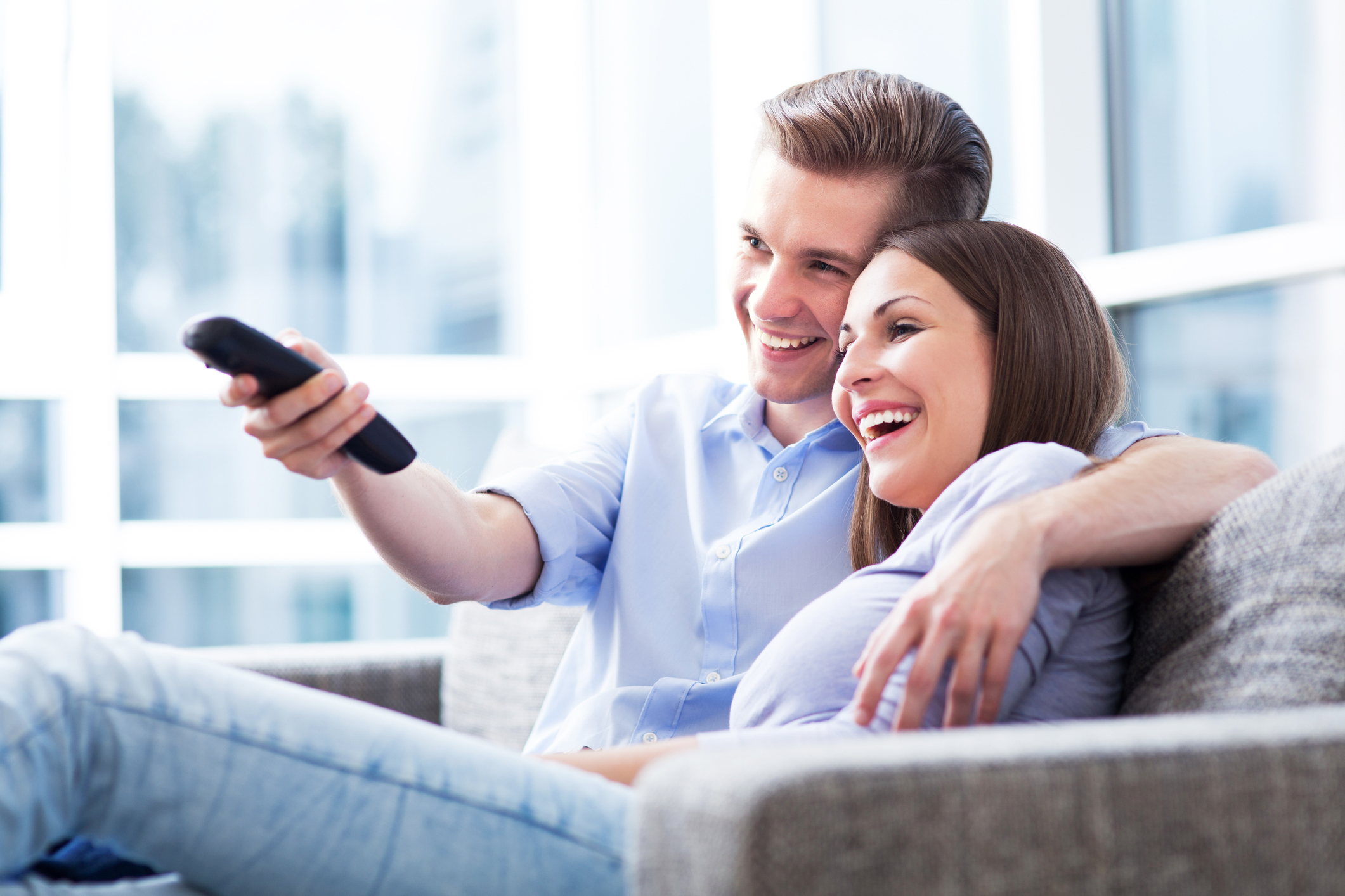 A smiling couple on a couch watches TV.