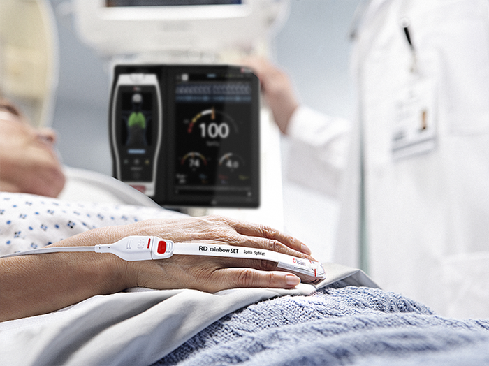 A patient in a hospital bed next to Masimo's RD rainbow set non-invasive monitoring system