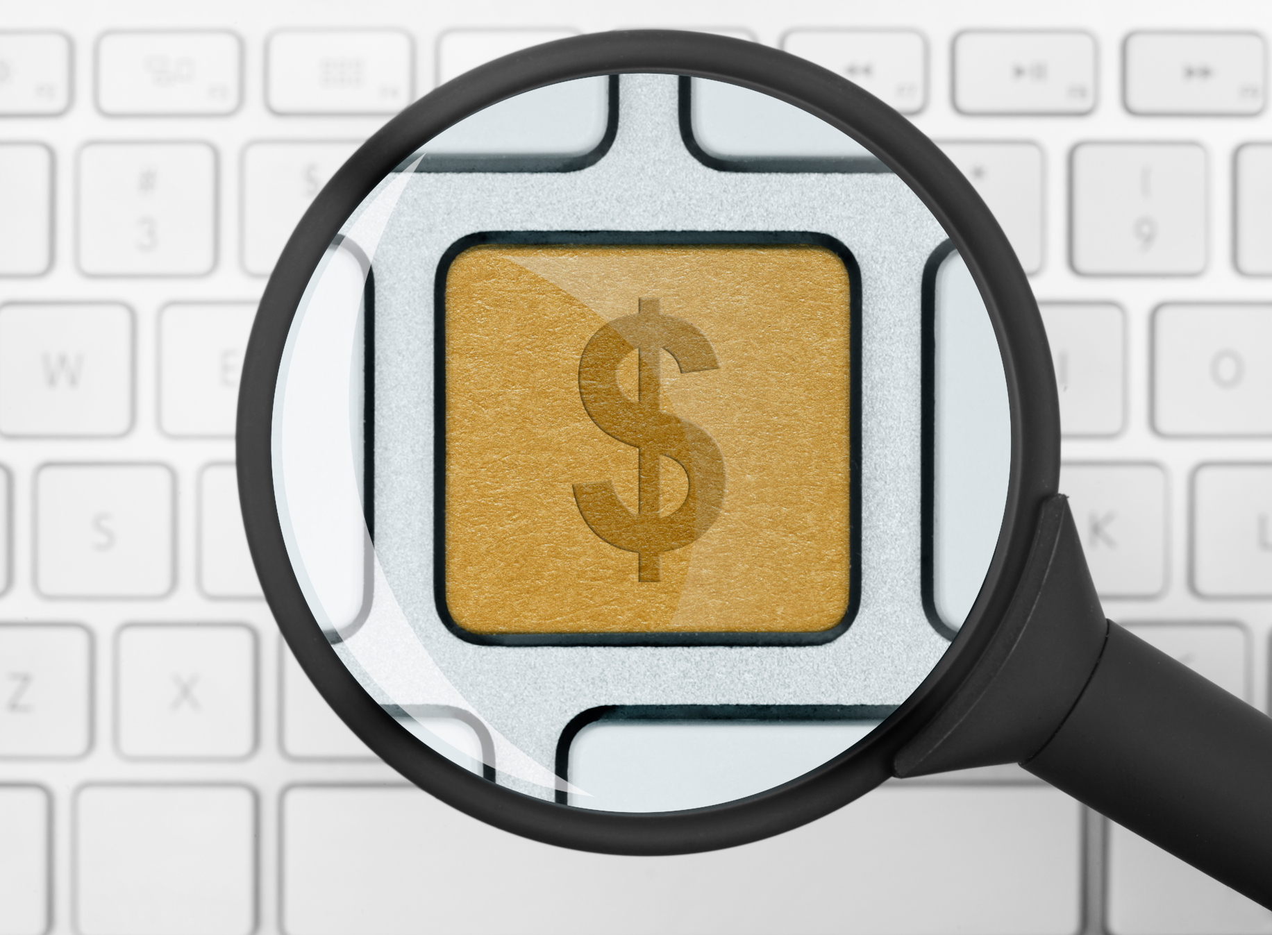 A white computer keyboard with a golden key featuring a dollar sign, highlighted under a magnifying glass.
