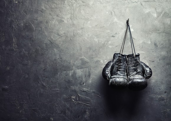 Old boxing gloves hang on nail on textured wall 