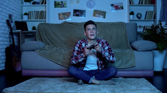 Boy sitting on a floor in front of a couch holding a game controller.