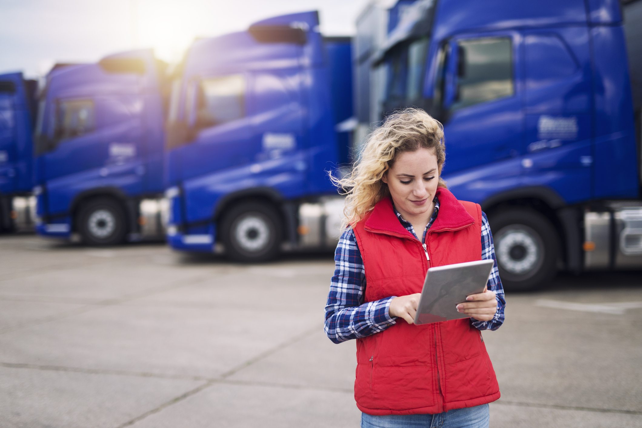 A woman using a tablet in front of a fleet of freight trucks