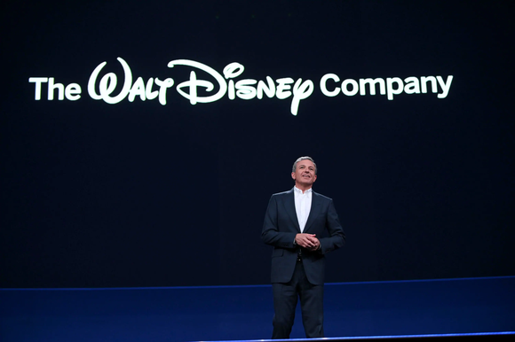 Disney CEO Bob Iger on stage with The Walt Disney Company logo =projected on a screen behind him.