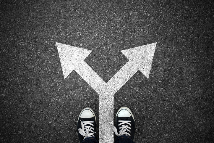 A pair of feet standing at a fork in an arrow drawn on the pavement.