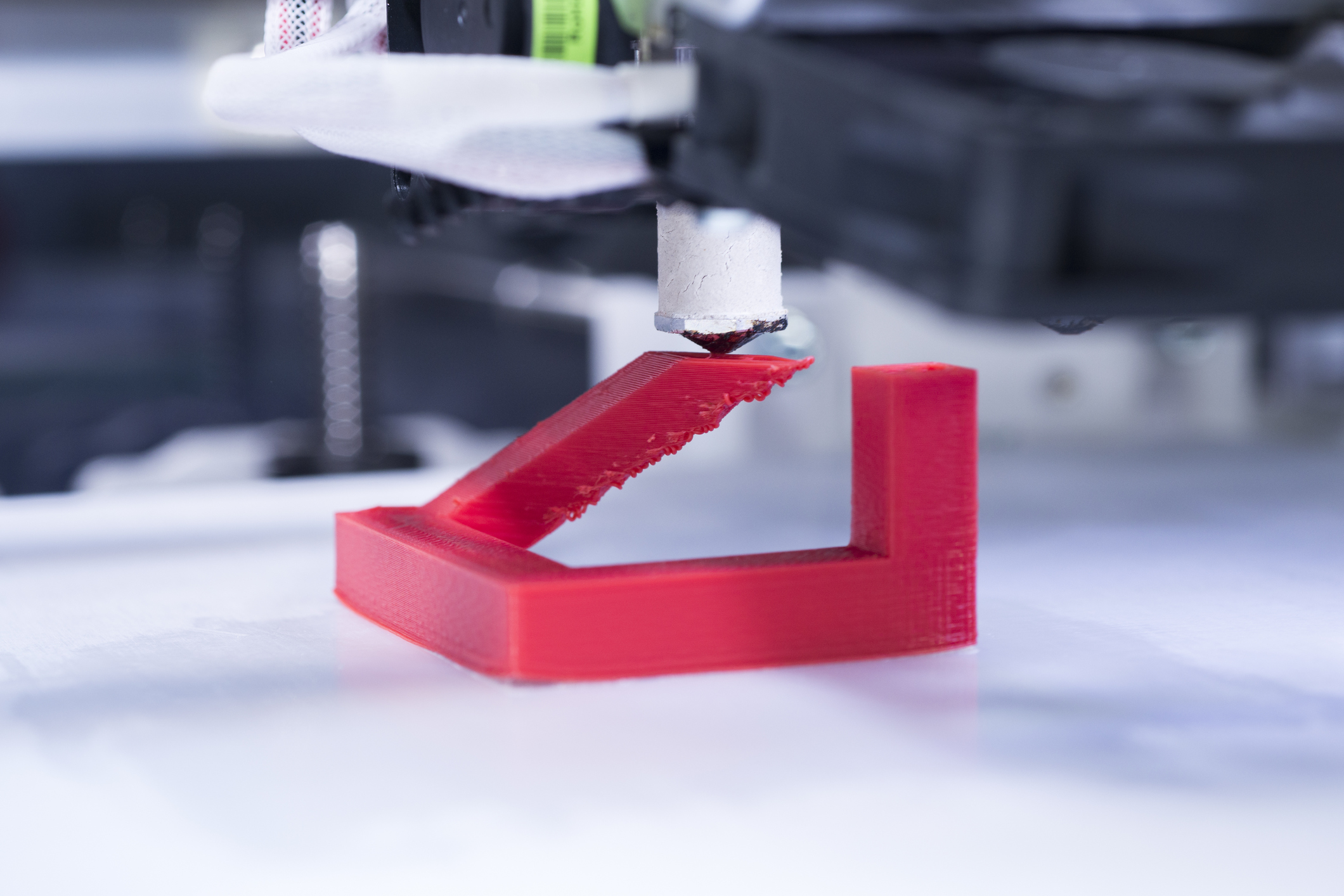 Close-up of a 3D printer with a blue surface printing a red plastic object.