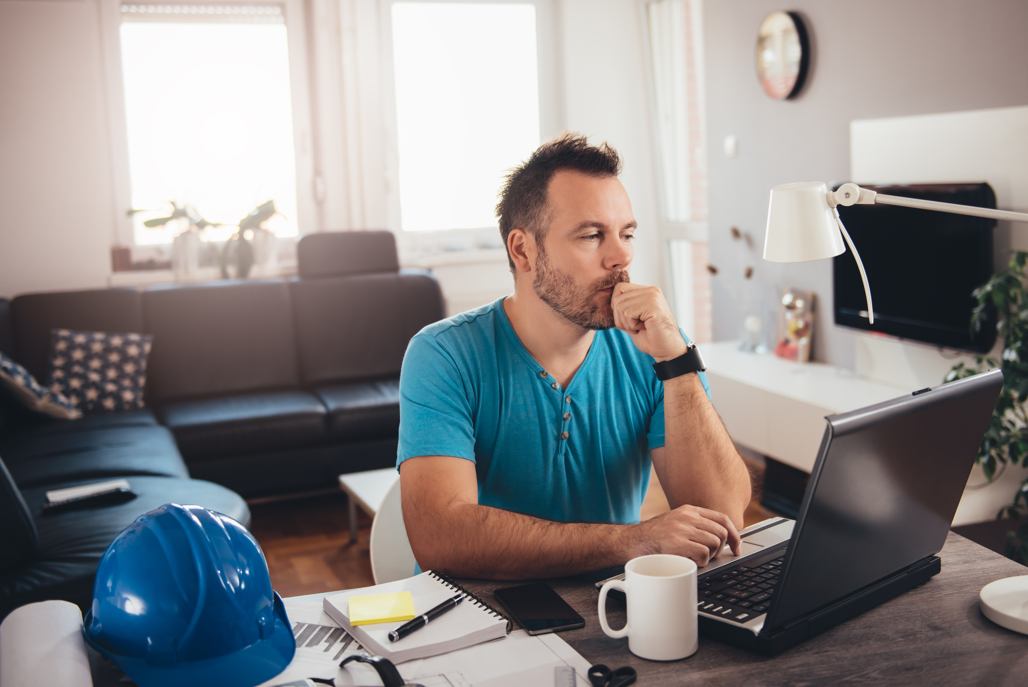 Man at laptop with serious expression resting chin on fist